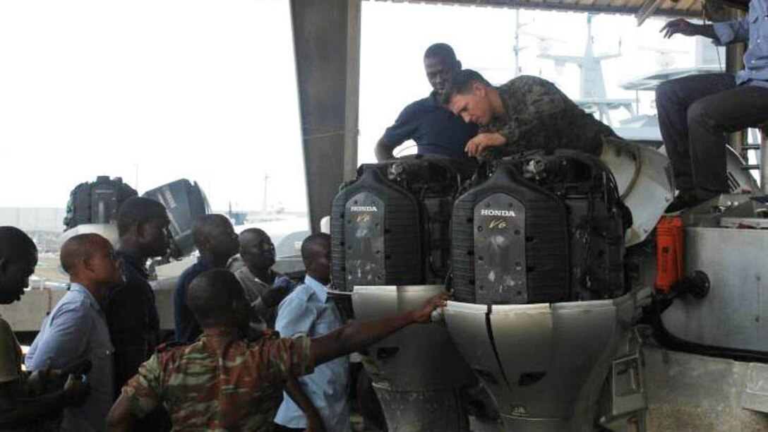 Petty Officer 2nd Class Joshua Araujo inspects the work conducted by members of the Beninese Navy in Cotonou, Benin, Nov. 20, 2014. Araujo, a Wichita Falls, Texas, native, is part of a team of Marines and Coast Guardsmen from SPMAGTF Crisis Response-Africa, working alongside the Beninese Navy, trading knowledge of mechanical tactics, techniques and procedural skills while conducting engine maintenance on Honda BF225 outboard engines. 