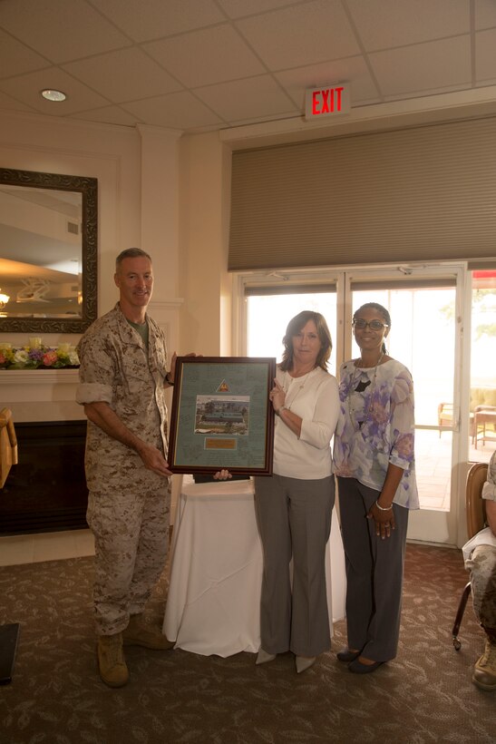 Col. Timothy Salmon (left), the commanding officer of Marine Corps Air Station New River and Lapeachtriss Turner(right), a colleague of Zerba, present Kathy Zerba (center) his former office management specialist and community liaison coordinator, with a gift during a surprise farewell celebration in her honor, at the Eagles Nest Officers’ Club aboard Marine Corps Air Station New River, July 10. Zerba is joining the staff of Naval Hospital Camp Lejeune after nine years of service at MCAS New River.