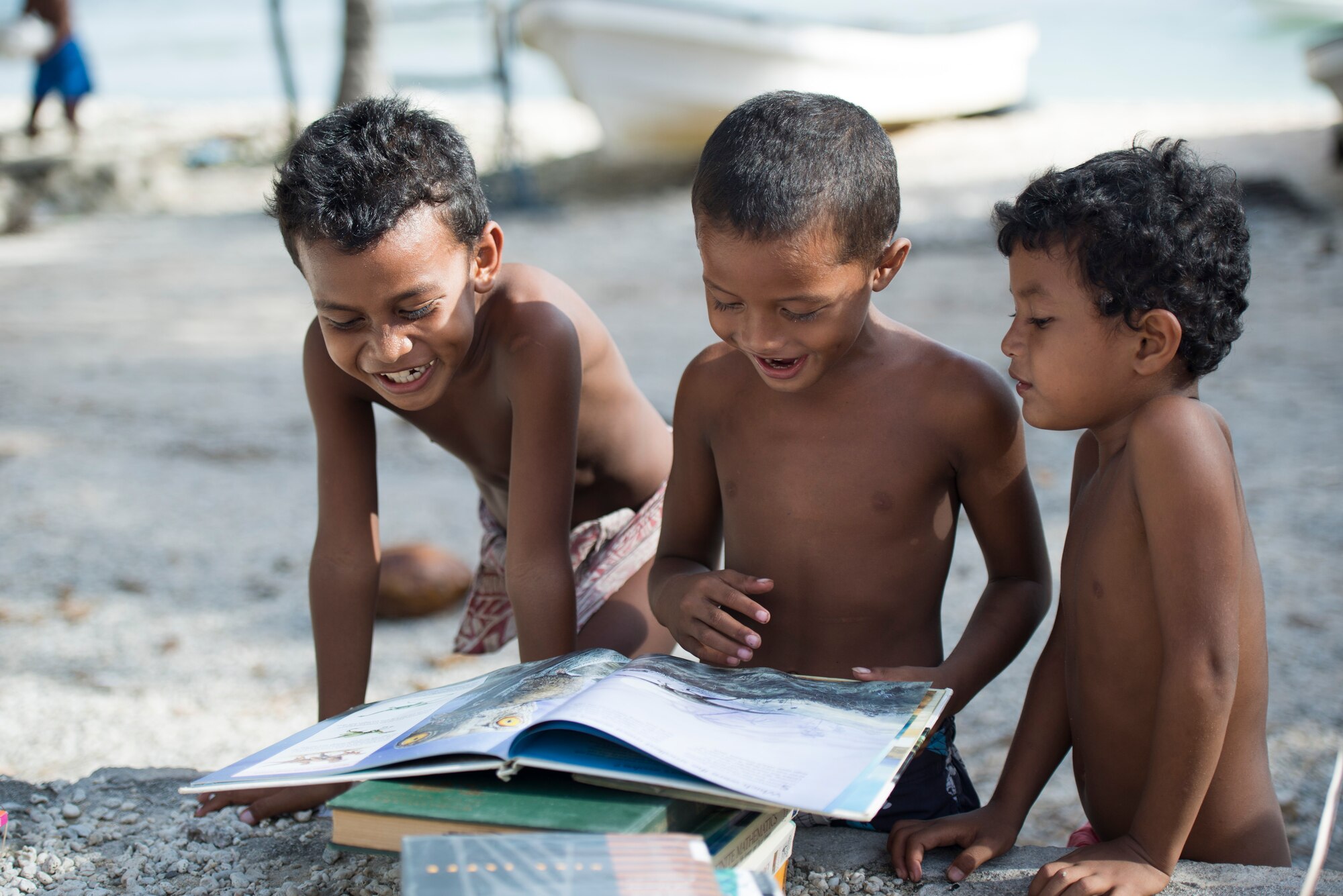 Children read about dinosaurs while looking through items received during Operation Christmas Drop at Ulithi Atoll, Micronesia, Dec. 9, 2014. Each year, with the help of OCD, children in Micronesia receive a gift, possibly a toy, which are a rarity on the islands. (U.S. Air Force photo by Staff Sgt. Cody H. Ramirez/Released)
