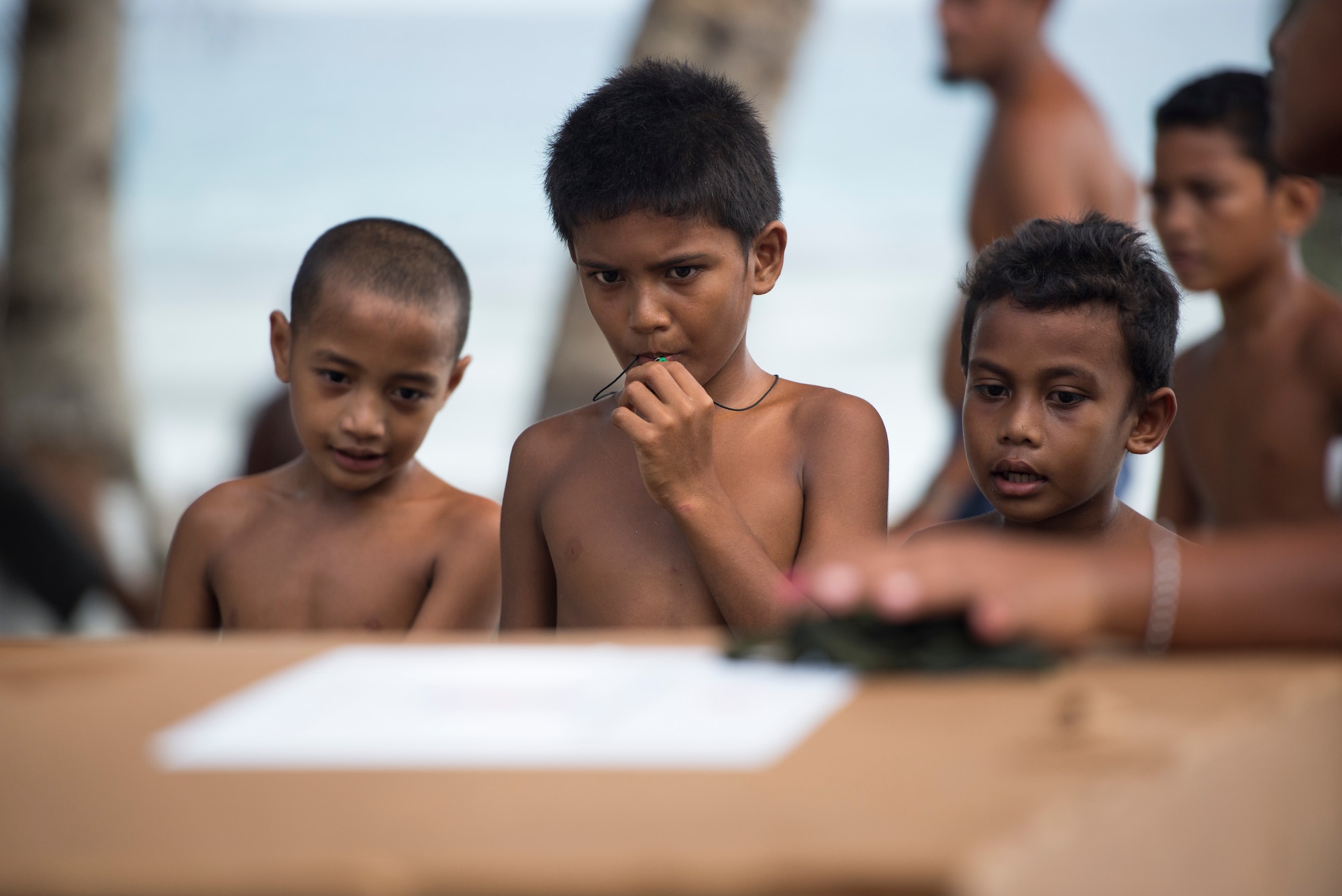 Boys watch as a package is opened during Operation Christmas Drop, Ulithi Atoll, Micronesia, Dec. 9, 2014. The package contents are shown, but gifts are stored and wrapped to be given to children on Dec. 25 in celebration of Christmas traditions. (U.S. Air Force photo by Staff Sgt. Cody H. Ramirez/Released)