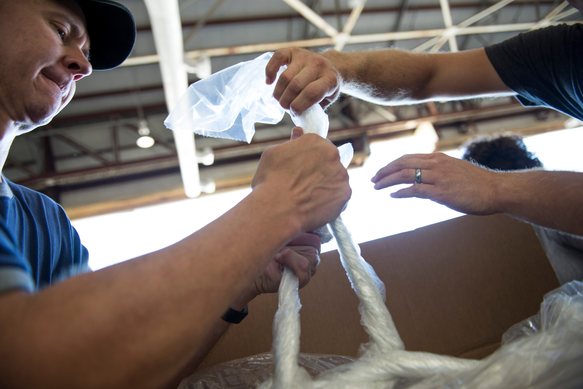 Two volunteers tie plastic bags while water- proofing donations during Operation Christmas Drop at Andersen Air Force Base, Guam, Dec. 06, 2014. The more than 50,000 pounds of donated goods were water- proofed to ensure rice and other items in the bundle do not spoil. (U.S. Air Force photo by Staﬀ Sgt. Cody H. Ramirez/Released)