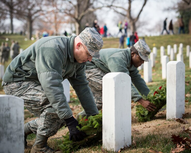 Tech. Sgt.  Richy Kruger and Senior Airman James Arredon, Airmen assigned to Air Force Mortuary Affairs Operations at Dover Air Force Base, Delaware, place holiday wreaths on two graves at Arlington National Cemetery, Dec. 13, 2014. Both Kruger and Arredon said that volunteering to honor the fallen at Arlington was a natural extension of their duties at AFMAO. (U.S. Air Force photo/Capt. Ray Geoffroy)