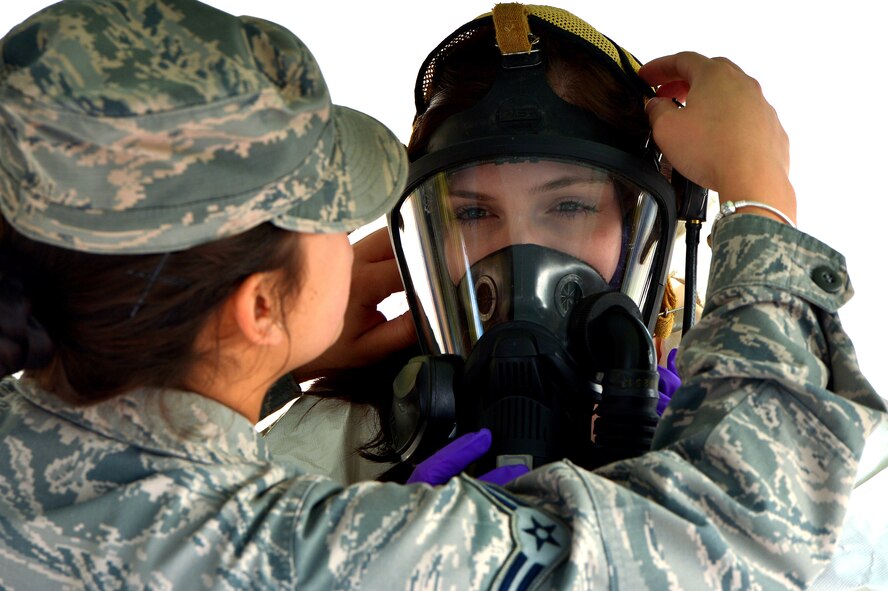 U.S. Air Force Airman 1st Class Cynthia Romero, 20th Civil Engineer Squadron emergency management apprentice aids Senior Airman Lauren Yancey, 20th Civil Engineer Squadron emergency management apprentice don her mask as she prepares to enter a simulated contamination zone during an integrated base emergency response capability exercise at Shaw Air Force Base, S.C., Dec. 9, 2014. Airmen who participated were challenged to respond to a simulated terrorist attack scenario and were evaluated on their performance. (U.S. Air Force photo by Staff Sgt. Kenny Holston/Released)