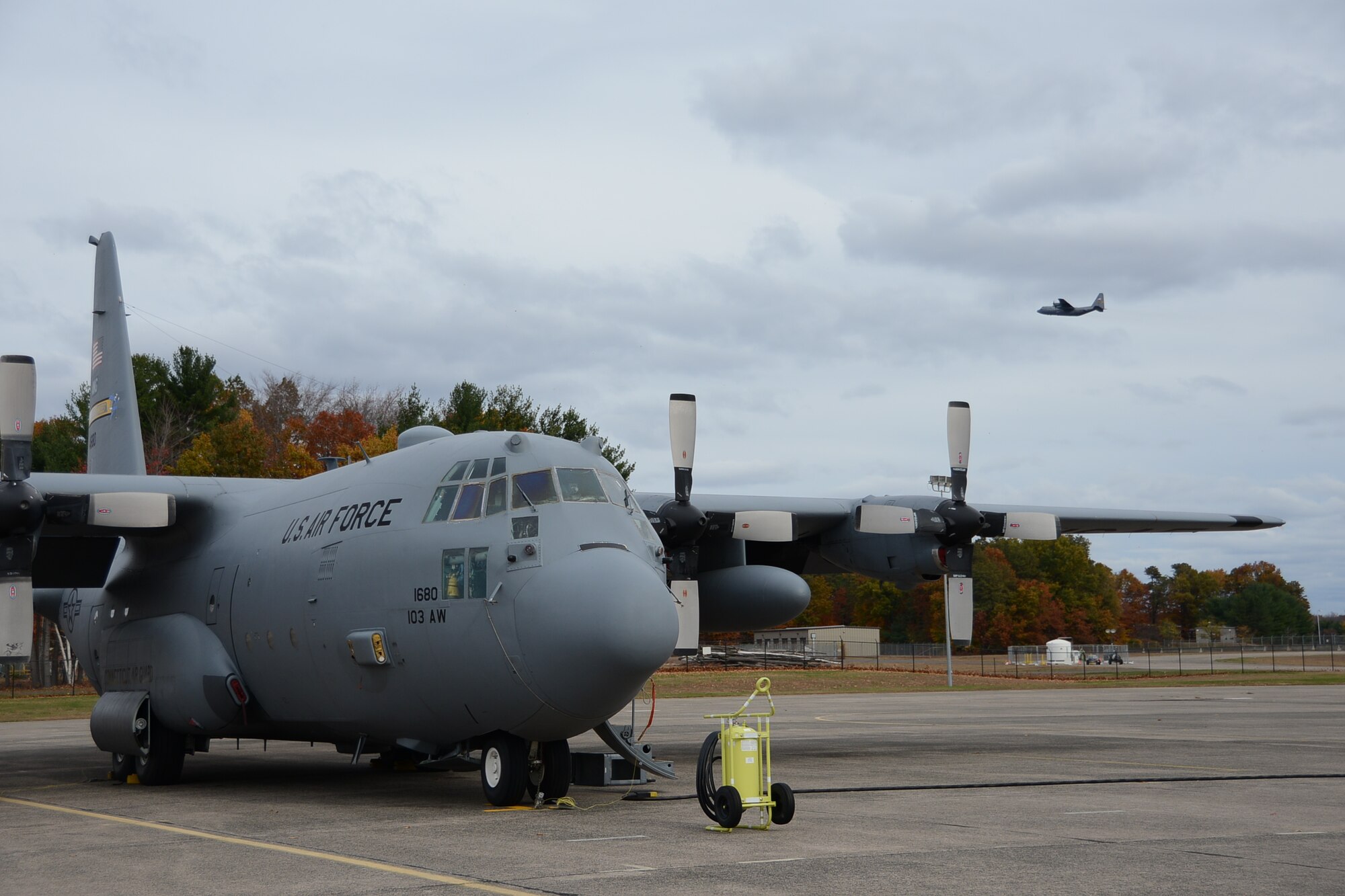 A C-130H Hercules aircraft assigned to the 103rd Airlift Wing takes off while another C-130H undergoes scheduled maintenance on the flightline below Nov. 1, 2014 at Bradley Air National Guard Base, East Granby, Conn.  Maintainers from the 103rd Maintenance Group configured the ascending aircraft, along with another, as part of the unit’s first C-130H engine generation exercise.  This exercise will be the first of many for the maintainers as different types of generation exercises are completed two to four times a year.  (U.S. Air National Guard photo by Maj. Bryon M. Turner)