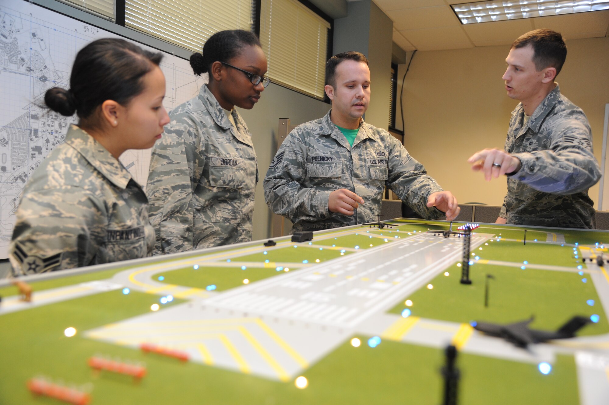 Airman 1st Class Kathryn Infantino and Airman Basic Marquise Jordan, 334th Training Squadron students, stand by while Staff Sgt. Courtney Polnicky, 334th TRS airfield management instructor, and Senior Airman Ryan Rathke, 334th TRS student, discuss the training capabilities the new model airfield training aid table offers Dec. 12, 2014, at Cody Hall, Keesler Air Force Base, Miss.  Utilizing the model, which is a scaled representation of an airfield, will increase understanding, productivity and efficiency in the classroom.  (U.S. Air Force photo by Kemberly Groue)