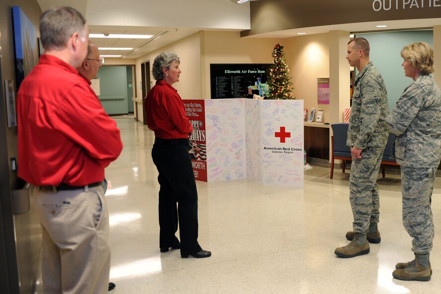 Michele Lewis, American Red Cross service to the armed forces director, explains the history behind the presentation of the American Red Cross holiday card to Col. Ty Neuman, 28th Bomb Wing vice commander, and Col. Susan Pietrykowski, 28th Medical Group commander, at Ellsworth Air Force Base, S.D., Dec. 12, 2014. This is the fifth year the Red Cross has presented a large card filled with holiday greetings from community members, which will be displayed in the lobby of the 28th MDG. (U.S. Air Force photo by Senior Airman Hailey R. Staker/Released)