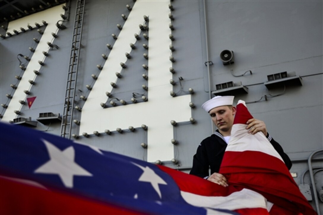 U.S. Seaman JaCade Jones folds the U.S. flag aboard the aircraft carrier USS John C. Stennis in the Pacific Ocean, Dec. 14, 2014.  