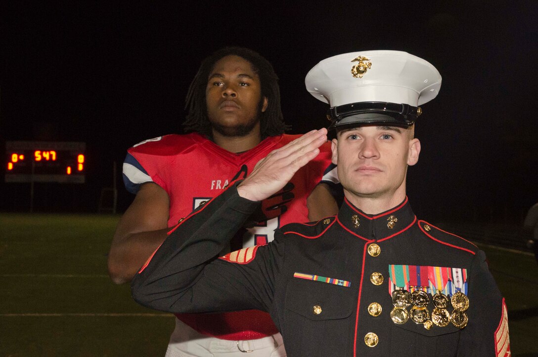 Sgt. Evan A. Page, a recruiter with Marine Corps Recruiting Station Baltimore, stands with Patrick Allen, an offensive tackle for Franklin High School, during the national anthem in Reisterstown, Maryland, Oct. 24. Allen has been selected to play in the 2015 Semper Fidelis All-American Bowl, which will be played in Carson, California in January. (U.S. Marine Corps photo by Sgt. Bryan Nygaard/Released)