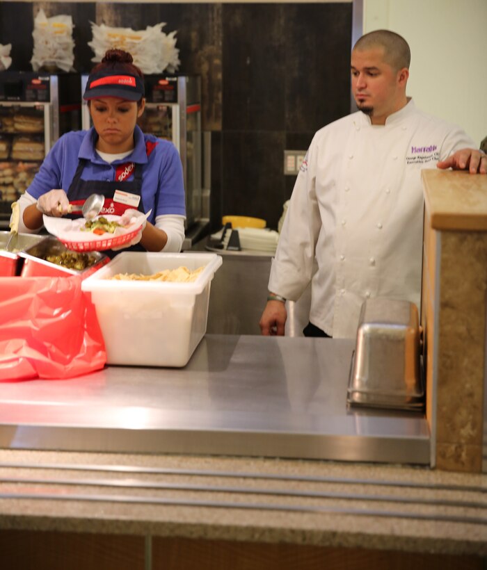 George Kapetsonis, Pink’s franchisee, teaches a Sodexo employee how to properly prepare a gourmet hot dog at Littleton mess hall, Dec. 2, 2014. Kapetsonis is also the sous chef at Harrah’s Resort Southern California. (Official Marine Corps photo by Lance Cpl. Medina Ayala-Lo/Released)