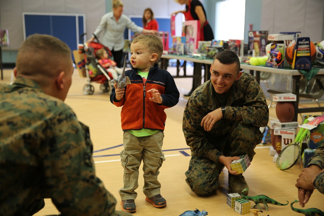 Max Hart, 3, son of Nicole Hart, military spouse, builds dinosaur formations with Marine Corps Communication-Electronics School students during Operation Homefront’s holiday toy distribution at the Community Center, Dec. 3, 2014. OHF is a financial assistance program for veterans and active duty service members. (Official Marine Corps photo by Lance Cpl. Medina Ayala-Lo/Released)