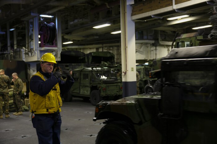 Petty Officer 2nd Class Ryan C. Meek, a boatswain’s mate with the USS Iwo Jima, signals to a Humvee driver in the well deck of the ship, Dec. 14. The 24th MEU embarked on the ships of the Iwo Jima Amphibious Ready Group for their 2015 deployment Dec. 12-14. The 24th MEU is scheduled to support operations in the 5th and 6th Fleet areas of responsibility.