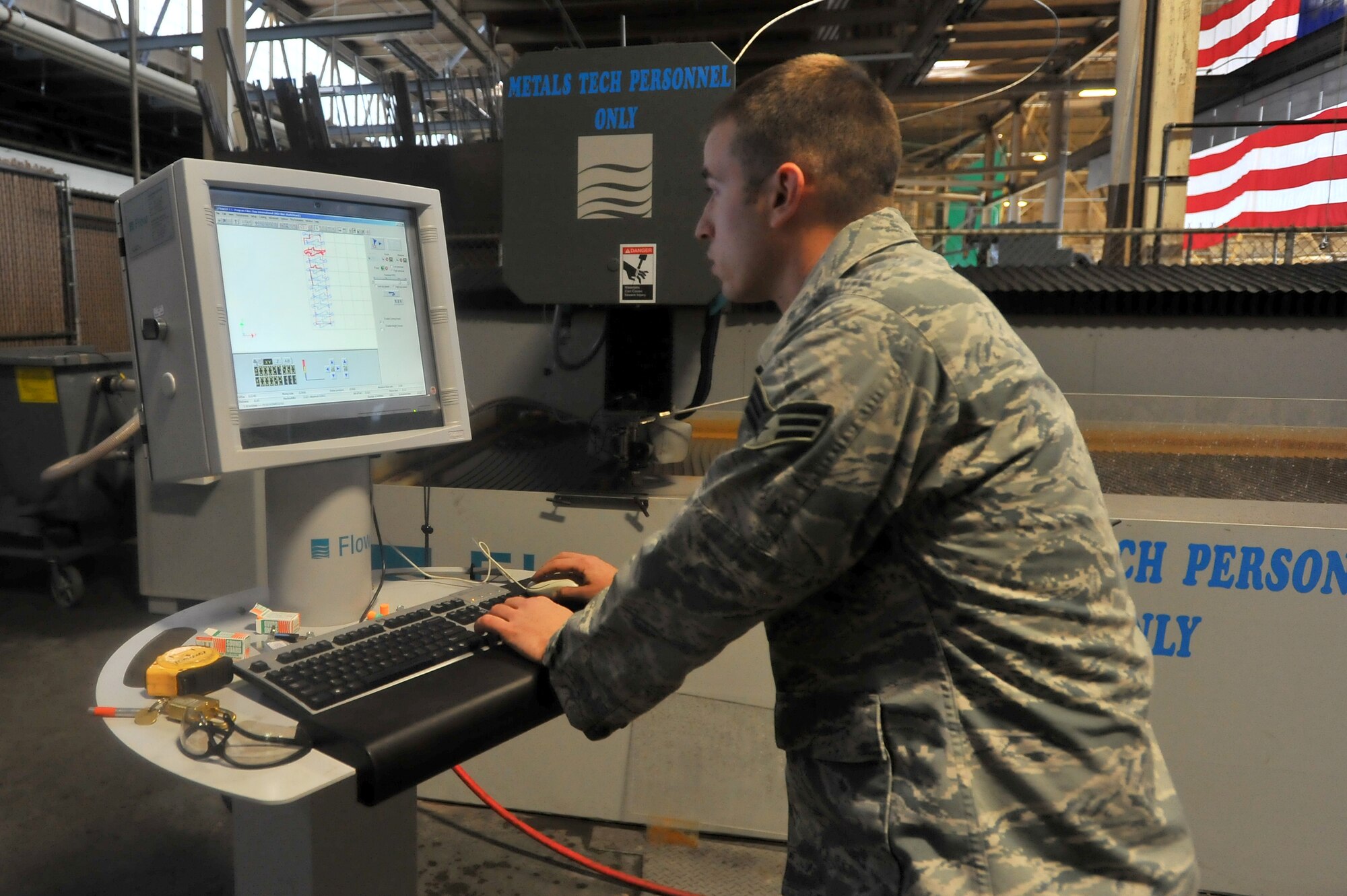 Senior Airman Jerry Brock, 92nd Maintenance Squadron aircraft metals technician, demonstrated the water jet to members of the 92nd Contracting Squadron during a tour Dec. 2, 2014, at Fairchild Air Force Base, Wash.  The water jet is a large piece of equipment recently installed in the 92 MXS metals shop that uses water with a garnet abrasive to precisely cut perfect and accurate lines in a variety of materials; saving time, manpower, resources and money. (U.S. Air Force photo/Staff Sgt. Veronica Montes)