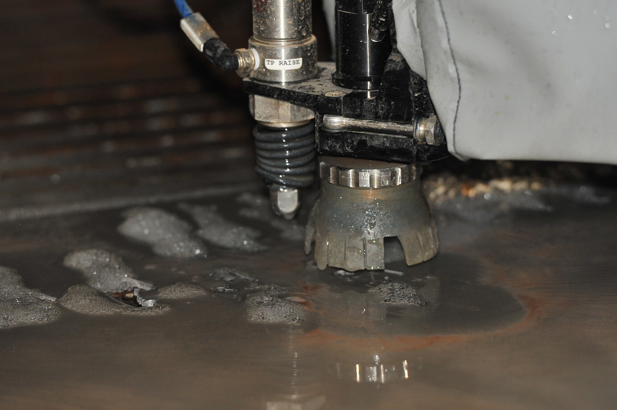 The water jet cuts precise shapes from a piece of metal while being demonstrated during a tour Dec. 2, 2014, at Fairchild Air Force Base, Wash.  The water jet is a large piece of equipment recently installed in the 92nd Maintenance Squadron metals shop that uses water with a garnet abrasive to precisely cut perfect and accurate lines in a variety of materials. (U.S. Air Force/Staff Sgt. Veronica Montes)
