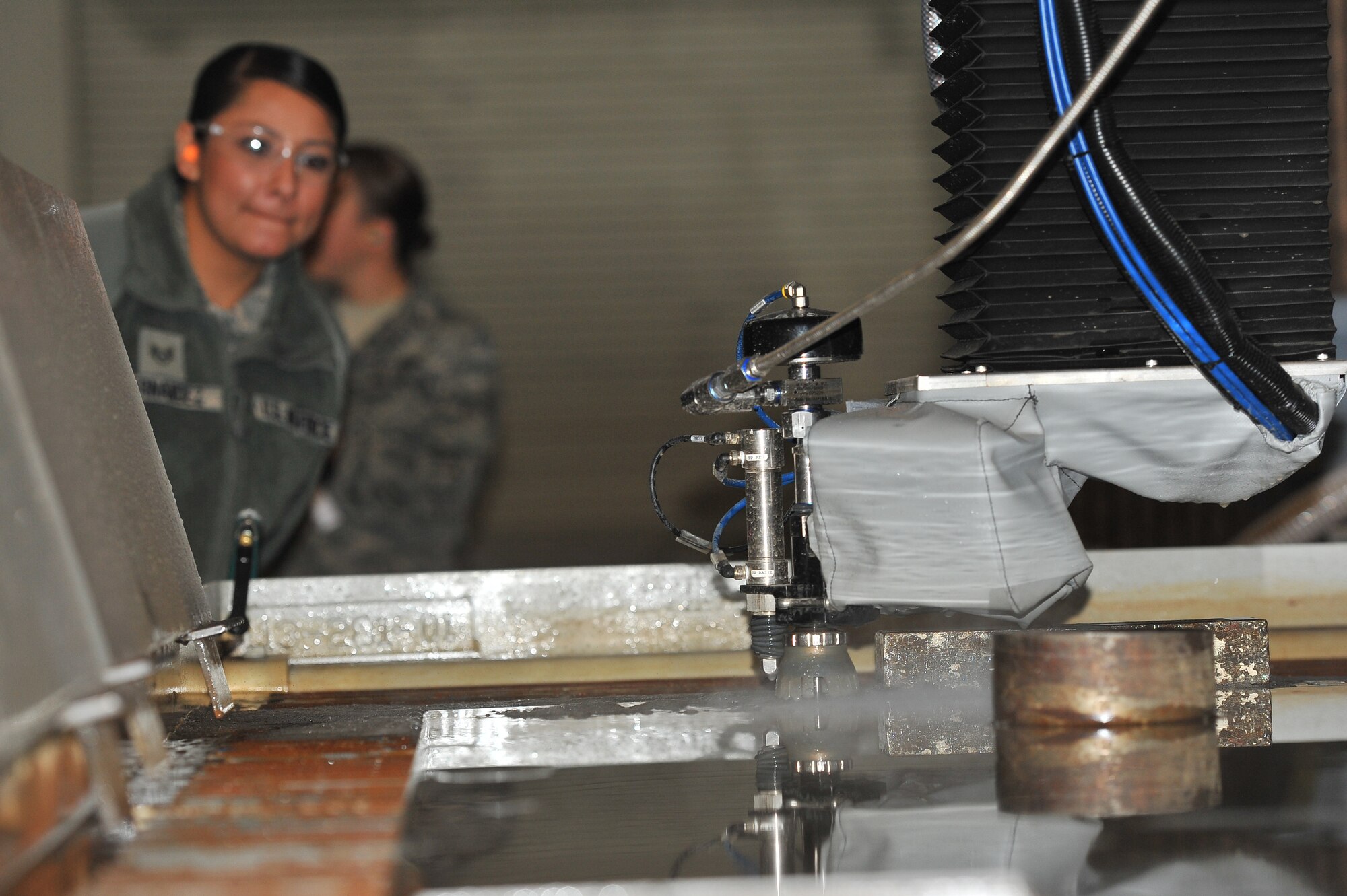The water jet cuts precise shapes from a piece of metal during a demonstration for the 92nd Contracting Squadron Dec. 2, 2014, at Fairchild Air Force Base, Wash.  The tour’s intent was to increase the understanding of the maintenance mission and show the contracting specialists firsthand the important role they play by purchasing equipment that saves time, money, and manpower for the 92nd Maintenance Group.  The water jet is a large piece of equipment recently installed in the 92nd Maintenance Squadron metals shop that uses water with a garnet abrasive to precisely cut perfect and accurate lines in a variety of materials, saving time, manpower, money, and resources. (U.S. Air Force/Staff Sgt. Veronica Montes)