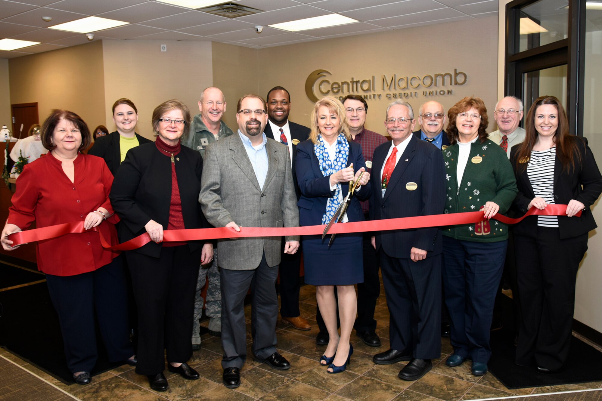 Drema Isaac, with scissors, president and CEO of the Central Macomb Credit Union, uses a large pair of scissors to cut the ribbon on a new location for the credit union at Selfridge Air National Guard Base, Mich., Dec. 18, 2014. The credit union first opened in 1957 as the Selfridge Air Force Base Credit Union. (U.S. Air National Guard photo by Terry Atwell)