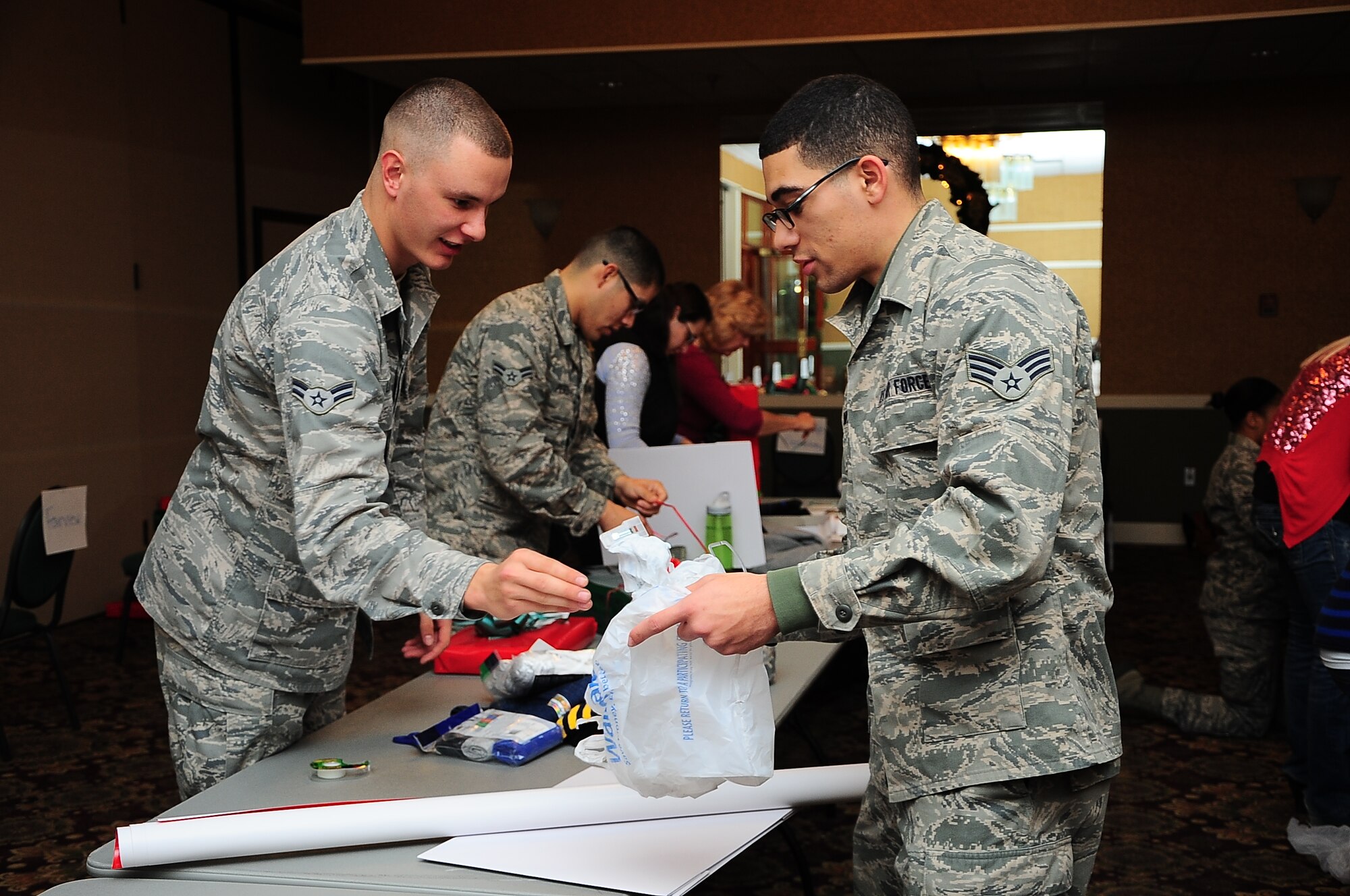 Airman 1st Class Bradley Litke, 14th Force Support Squadron Force Management Apprentice, and Senior Airman Ronnie Smith, 14th Operations Support Squadron Airfield Systems Journeyman, wrap presents during the Happy Fund Shop and Wrap event Dec. 18 in the Columbus Club. Local area teachers nominate children to receive gifts from the fund. (U.S. Air Force Photo/Senior Airman Stephanie Englar)