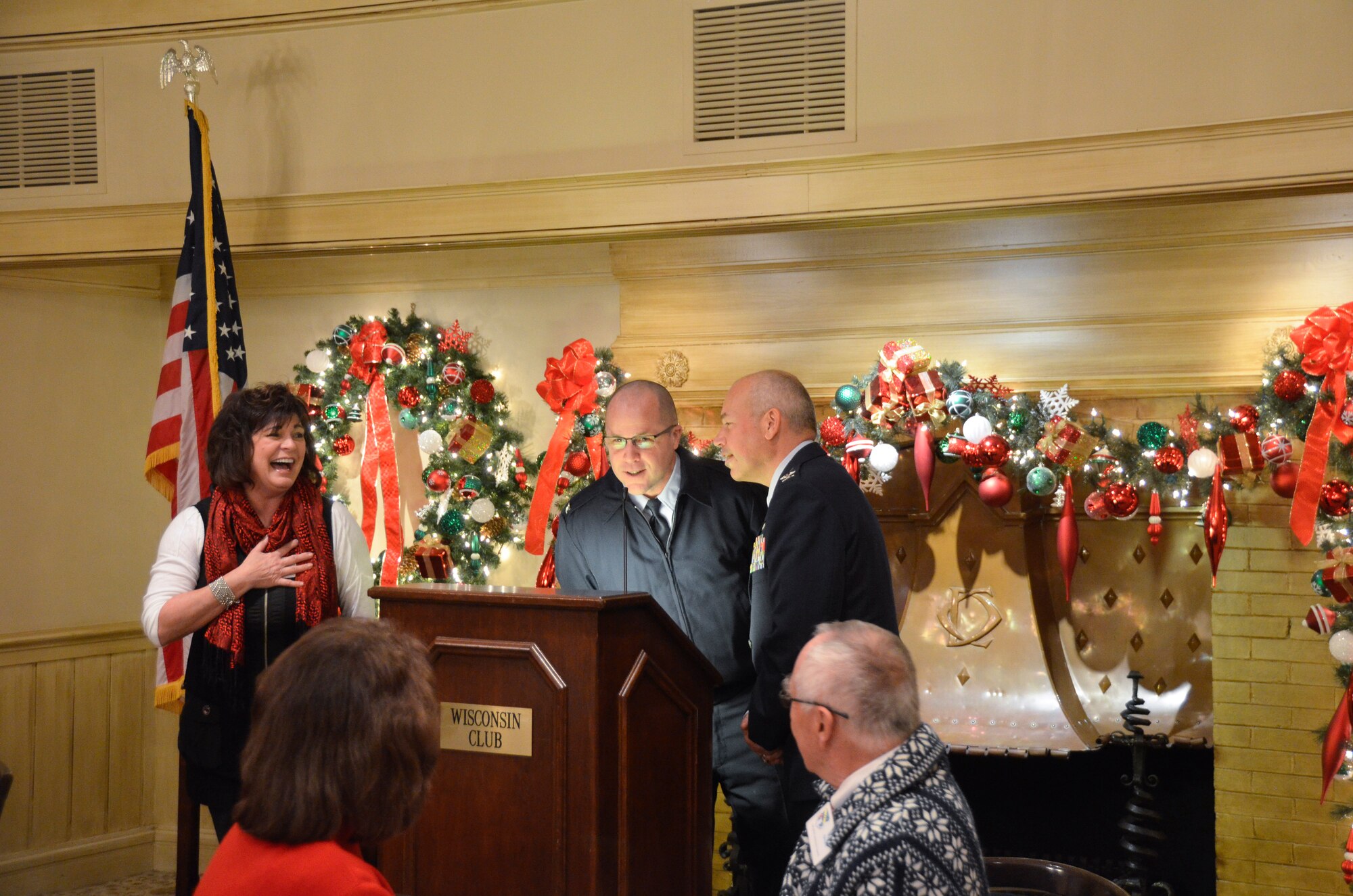 Janine Sijan Rozina laughs aloud as she watches Col. Daniel S. Yenchesky, wing commander and Col. James V. Locke,  vice commander of the 128th Air Refueling Wing, sing their rendition of “Five Golden Rings” during a 128th Community Council general membership meeting held at the Wisconsin Club, Milwaukee, Dec. 12, 2014. A tradition for the general membership is to close the December meeting with the singing of the  “Twelve Days of Christmas.” (U.S. Air National Guard photo by Maj. Sherri A. Hrovatin/Released)