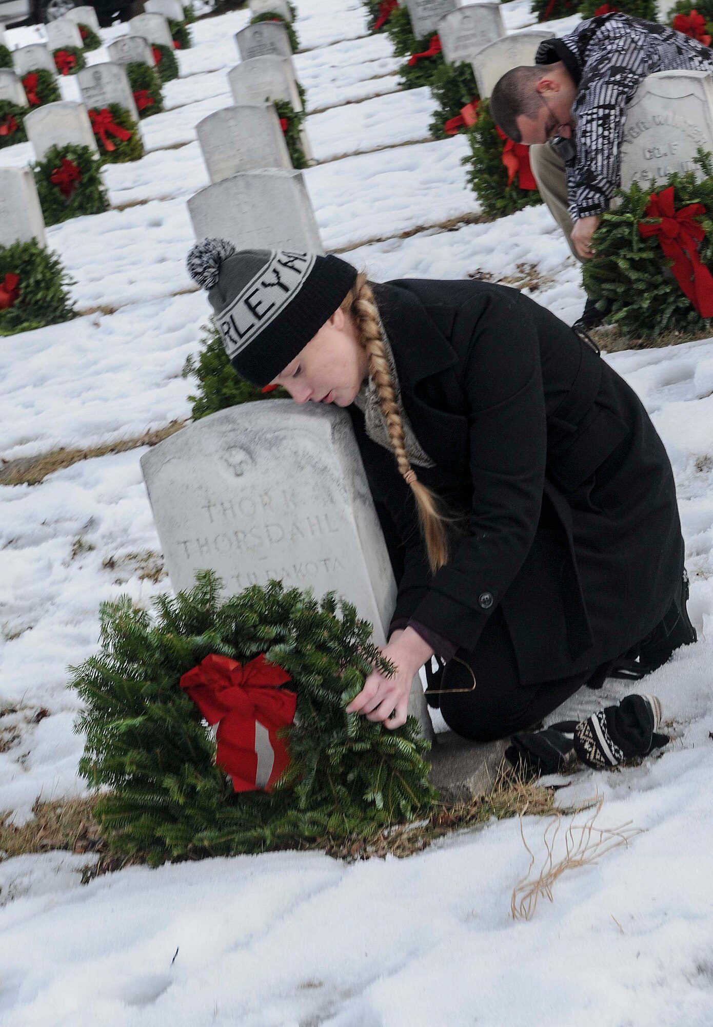 Staff Sgt. Kelsey Villarreal, 5th Maintenance Group, ties string to a wreath that was placed at the headstone of a veteran during a ceremony commemorating national Wreaths Across America Day at Rosehill Memorial Park Cemetery in Minot, N.D., Dec. 13, 2014. Villarreal remained behind with a handful of other volunteers after the ceremony to secure the wreaths so that they would not be knocked down or blown away by the wind. (U.S. Air Force photo/Senior Airman Stephanie Morris)