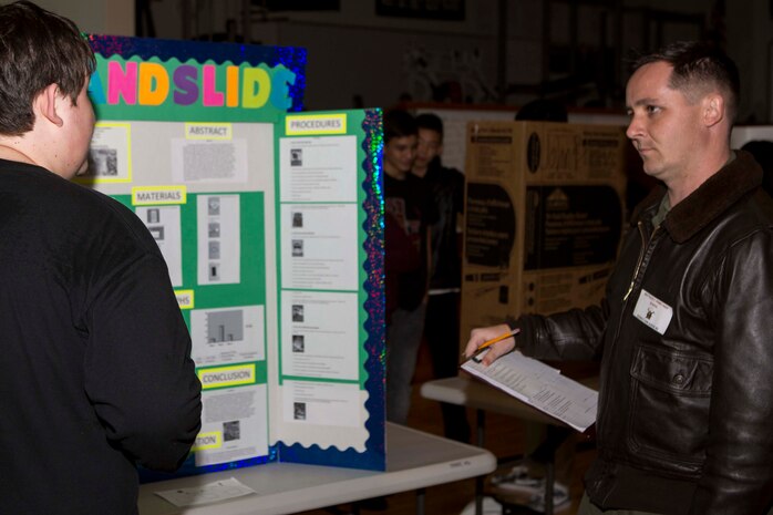 Capt. Benjamin Baldwin, a weapon systems officer with Marine All-Weather Fighter Attack Squadron 242 and a judge for Matthew C. Perry High School’s science fair, listens to a student as he explains his project inside the high school gymnasium, Dec. 18, 2014, aboard Marine Corps Air Station Iwakuni, Japan. The science fair is part of the school’s Science, Technology, Engineering and Mathematics (STEM) initiative, which presented students with an opportunity to practice the scientific method. 