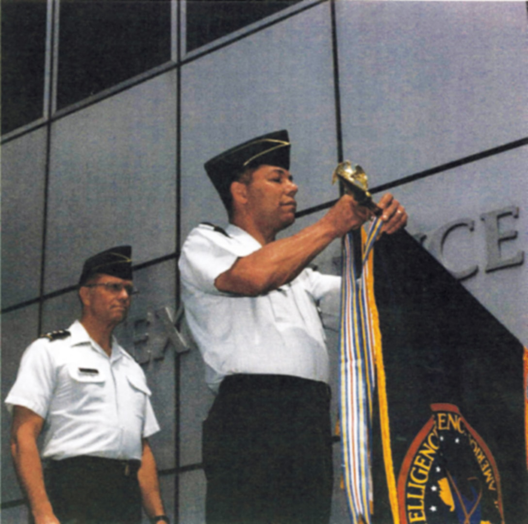 DIA Director Lieutenant General Harry Soyster, USA, looks on as Chairman of the Joint Chiefs of Staff General Colin Powell places the streamer for DIA's second Joint Meritorius Unit Award. DIA received this award in 1991 for its performance during Operations DESERT SHIELD and DESERT STORM.