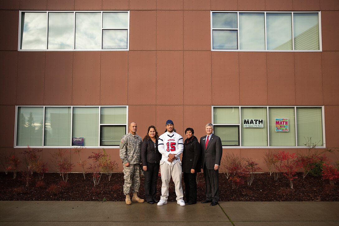 Benning Potoae (center), a defensive end for the Lakes High School Lancers varsity football team and 18-year-old native of Dupont, Washington, stands alongside his parents, Army 1st Sgt. Aleki Potoae and his wife Sherry (left), and Lakewood Councilwoman Mary Moss and Mayor Don Anderson, after receiving his 2015 Semper Fidelis All-American Bowl jersey from Seattle-area Marines at Lakes High School in Lakewood, Washington, Dec. 16, 2014. Potoae is among approximately 100 student athletes from across the nation selected to participate in the game at the StubHub Center in Carson, Calif., Jan. 4, 2015. He joins cornerback Austin Joyner from Marysville-Pilchuck High School and offensive tackle Shane Lemieux from Yakima’s West Valley High School as the Washington State players selected for the 2015 game. (U.S. Marine Corps photo by Sgt. Reece Lodder / Released)