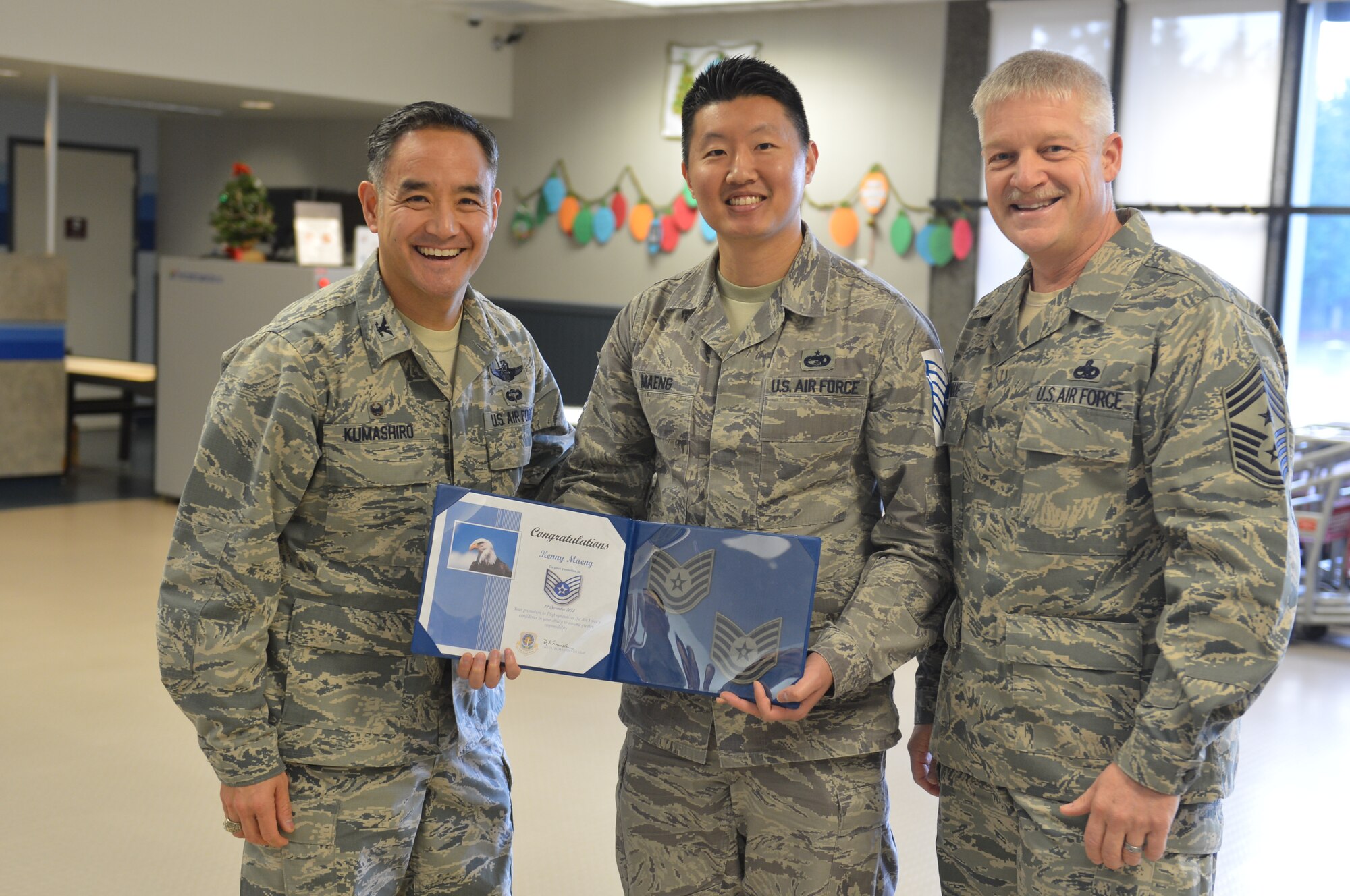 Col. David Kumashiro (left), 62nd Airlift Wing commander and Chief Master Sgt. Gordon Drake, 62nd AW Command Chief (right), pause for a photo with Tech. Sgt. Kenny Maeng, 62nd Aerial Port Squadron passenger services shift supervisor at the McChord Field Passenger Terminal, Dec. 19, 2014 at Joint Base Lewis-McChord. Maeng was surprised when the commander and command chief showed up to a maintenance quarterly awards ceremony and was notified of his selection as one of two 18th Air Force Airmen presented stripes as part of the Stripes for Exceptional Performers program. (U.S. Air Force photo/Master Sgt. Todd Wivell)