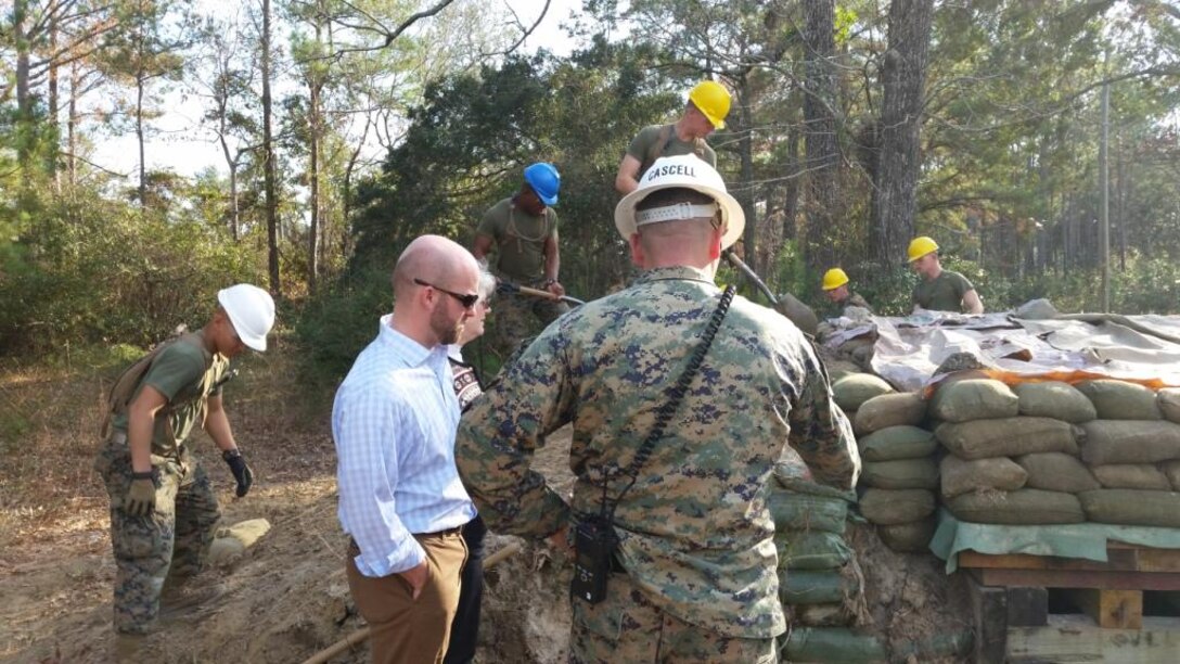 On December 16, 2014, Ryan Crumpler and Vickie Plunkett, both Professional Staff Members on the House Armed Services Committee, visited Marine Corps Engineer School in order to gather information regarding enlisted entry level training.  Here they are seen getting a brief from GySgt Cascell at the survivability training site.
