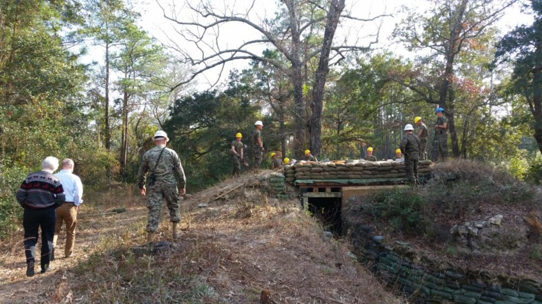 On December 16, 2014, Ryan Crumpler and Vickie Plunkett, both Professional Staff Members on the House Armed Services Committee, visited Marine Corps Engineer School in order to gather information regarding enlisted entry level training.  Here they are seen getting a brief from GySgt Cascell at the survivability training site.