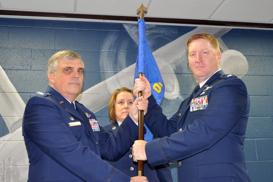 YOUNGSTOWN AIR RESERVE STATION, Ohio – Air Force Reserve Col. Bill Phillips, 910th Operations Group commander, hands the 910th Operations Support Squadron (OSS) guidon, or unit flag, to Lt. Col. Roark D. Endlich during an Assumption of Command ceremony held here, Dec. 6, 2014. Master Sgt. Michelle Mariacher, 910th OSS first sergeant, looks on as the guidon is transferred during the ceremony. The 910th OSS deploys mission ready combat tactics, intelligence, aircrew flight equipment and current operations personnel in support of worldwide Department of Defense wartime, peacetime and humanitarian airlift as well as aerial spray requirements. The squadron maximizes airlift efficiency and aircrew survivability in achieving the 910th Airlift Wing’s mission to Deploy, Deliver, Defend and the wing’s vision of bring an Operational Force for Rapid Global Mobility with integrated and sustainable capabilities supporting our National Security. U.S. Air Force photo by Master Sgt. Bob Barko Jr.