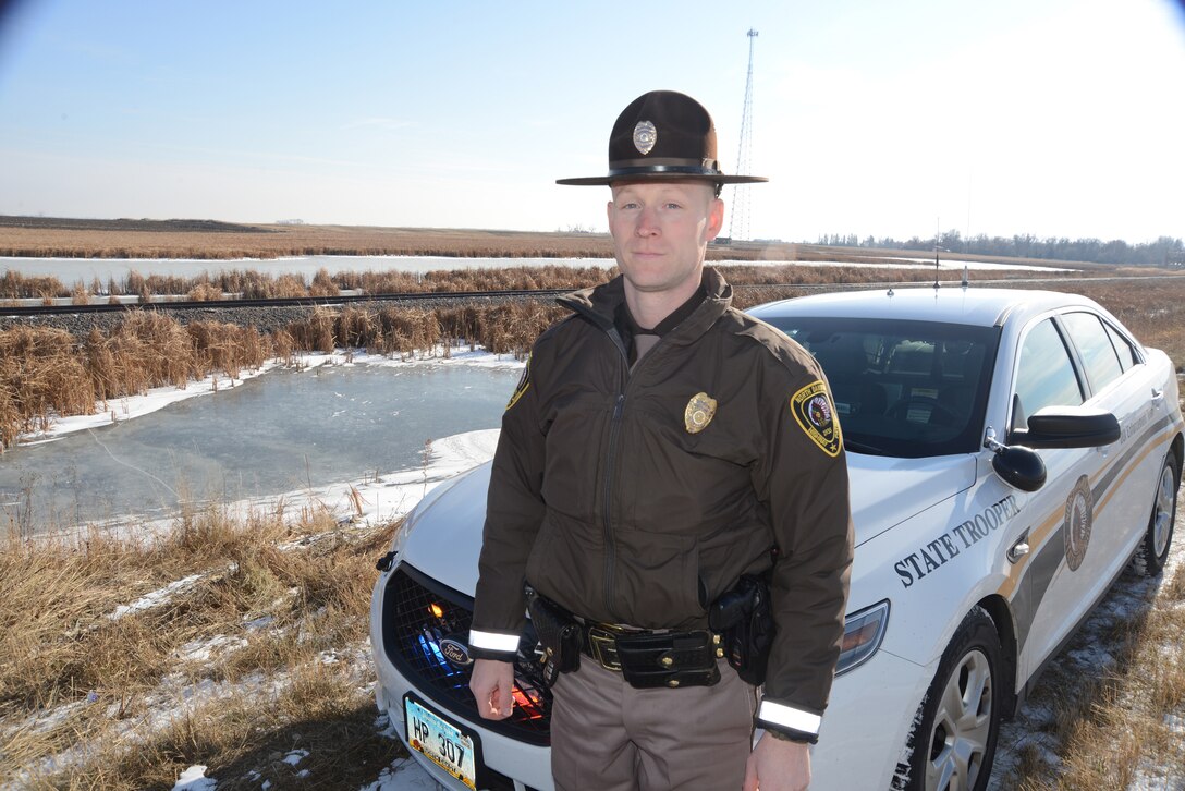 Master Sgt. Grant Lonski, of the 119th Security Forces Squadron, visits the accident scene that he responded to while performing his full-time North Dakota Highway Patrol duties near Churchs Ferry, North Dakota a week prior to the Nov. 18, 2014 return visit. Lonski was able to pull 81-year old accident victim Merti Kurtti from freezing cold water in the ditch behind him in the photo. (U.S. Air National Guard photo by Senior Master Sgt. David H. Lipp/Released)