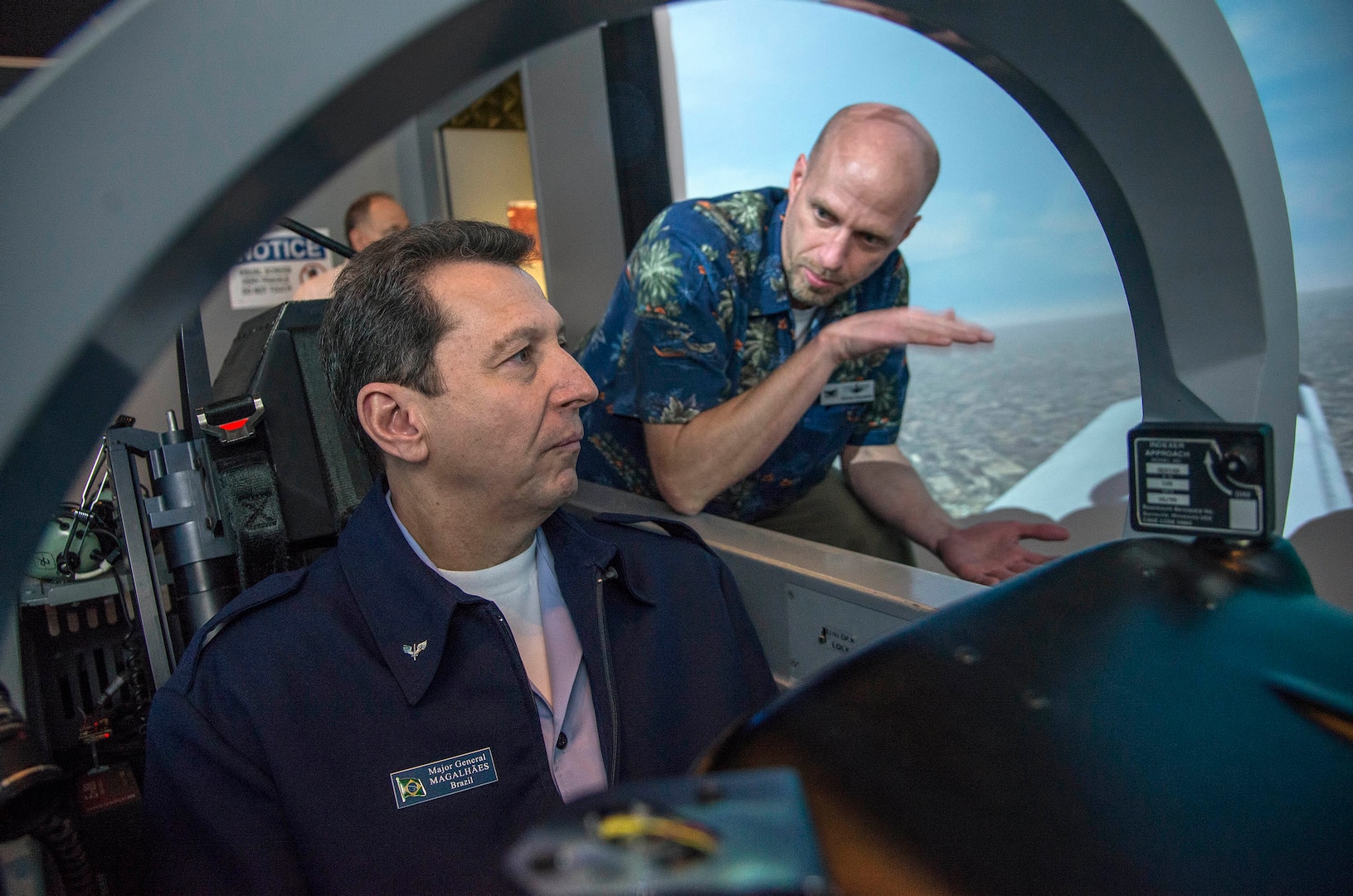 Kevin Coleman (right), 12th Operations Support Squadron flight simulator instructor, instructs Brazilian air force Maj. Gen. Ricardo Magalhaes, defense and air attaché, on flying in a T-6 simulator Dec. 11, 2014 during a visit to the 435th Flying Training Squadron at Joint Base San Antonio-Randolph, Texas. The flight simulator creates a realistic environment for students to experience flying a plane. (U.S. Air Force photo by Johnny Saldivar) 