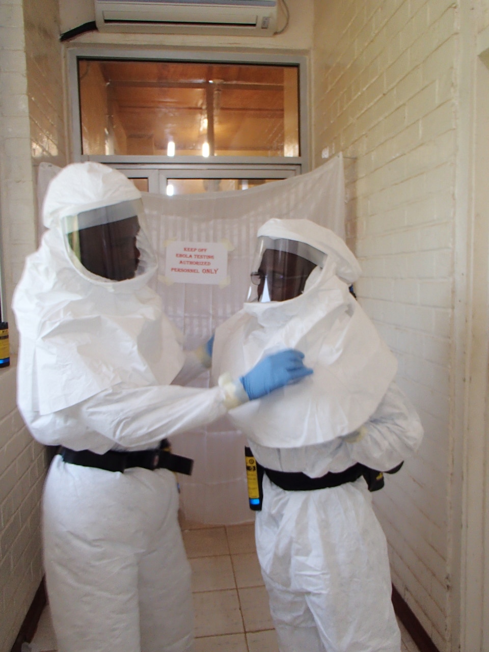 Aaron Momolu, left, and Lawrence Fakoli, Liberian laboratory technicians at National Public Health Reference Laboratory, put on personal protective equipment before entering a containment area to test samples. U.S. Army photo by Dr. Randal J. Schoepp: