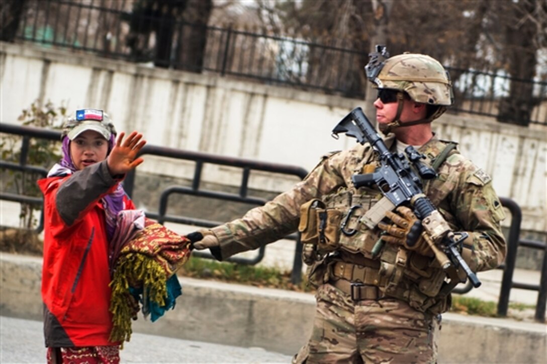 A U.S. soldier provides security as an Afghan child waves to International Security Assistance Force members as they pass by in Kabul, Afghanistan, Dec. 20, 2014.