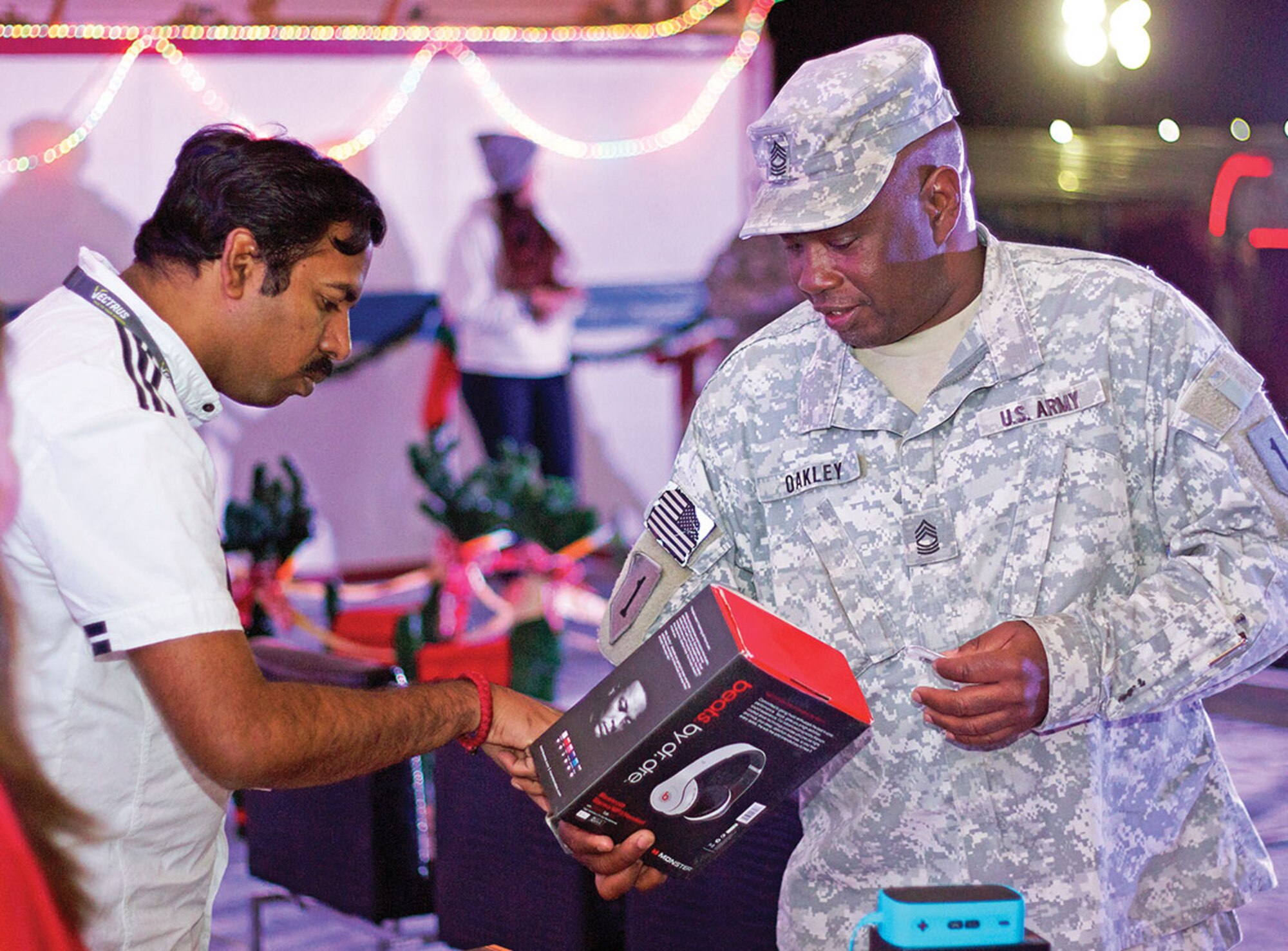 Mandar Pal, an MWR staff member (left) talks to Master Sgt. Timothy Oakley, support operation NCOIC, HHC, 1st ABCT (right) about the headset he won during the Christmas tree lighting and winter carnival Dec. 3 at MWR at Camp Buehring, Kuwait. The event was co-sponsored by Camp Buehring MWR and ASG-Kuwait to usher in the holiday season.  
