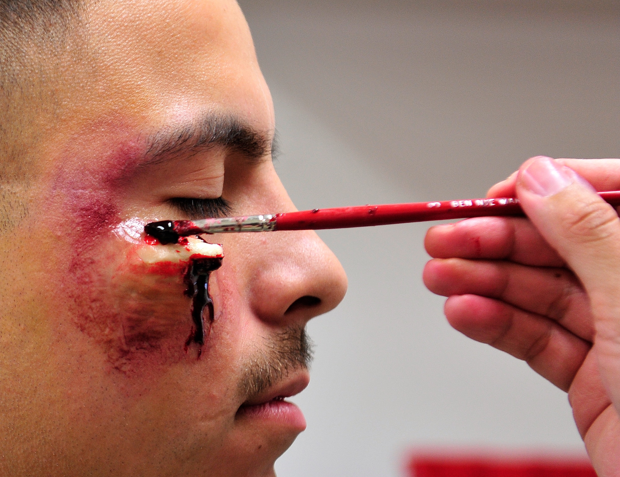 Moulage make-up is applied to U.S. Air Force Airman 1st Class Armand Villarreal, 18th Medical Operations Squadron medical technician, during disaster team training on Kadena Air Base, Japan, Dec. 18, 2014. Villarreal was a volunteer moulage victim being made-up for a disaster team training to he will help add realism to the triage process. (U.S. Air Force photo by Naoto Anazawa)