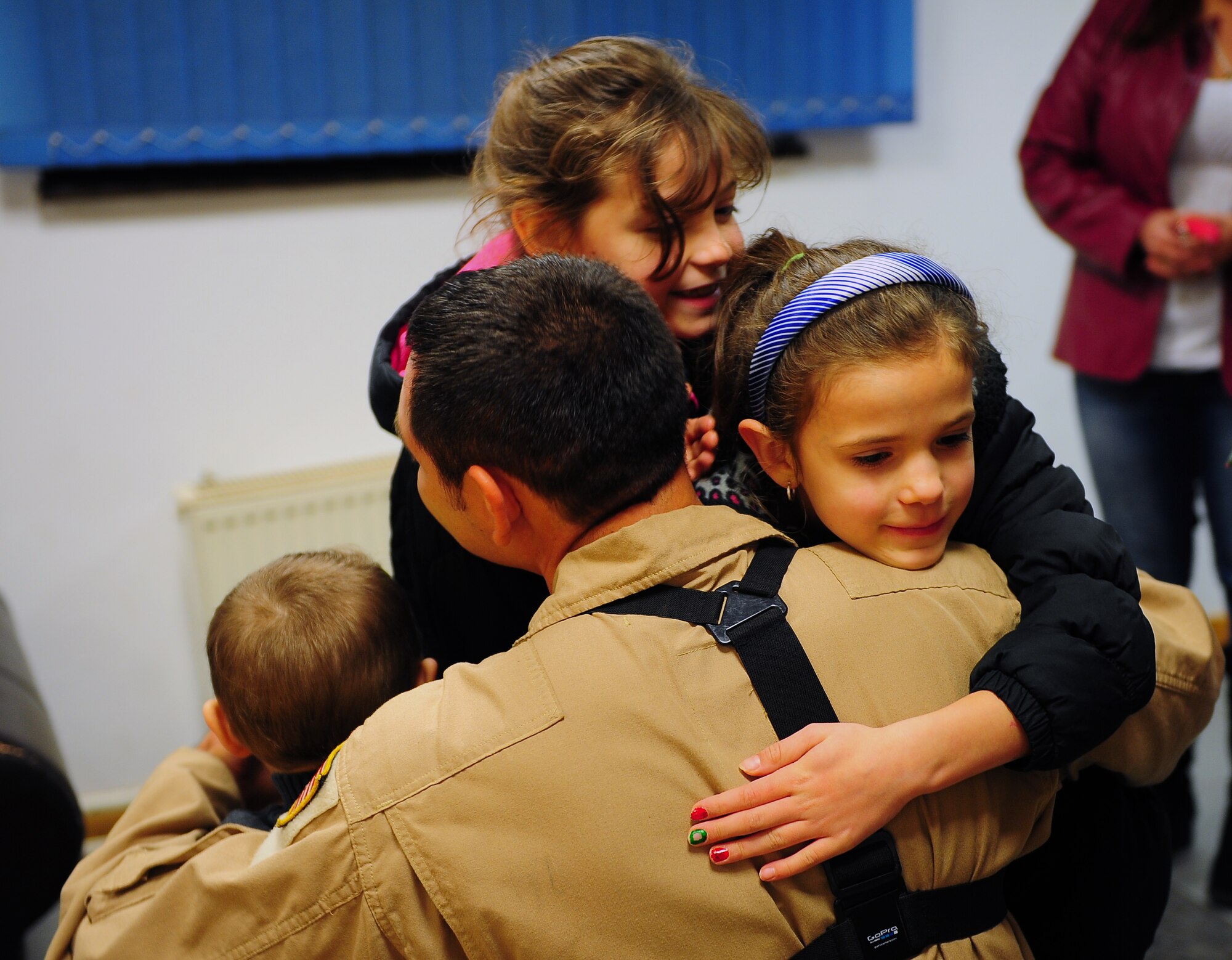 Rain, Faith and James Anderson embrace their father, Staff Sgt. Richard Anderson, 37th Airlift Squadron loadmaster, after he burst out of a gift-wrapped box surprising them right before Christmas, Dec. 23, 2014 at Ramstein Air Base, Germany. Anderson’s wife, Amy, meticulously planned the holiday surprise with the help of several members of the 37th AS and their families. (U.S. Air Force photo/Staff Sgt. Kris Levasseur)