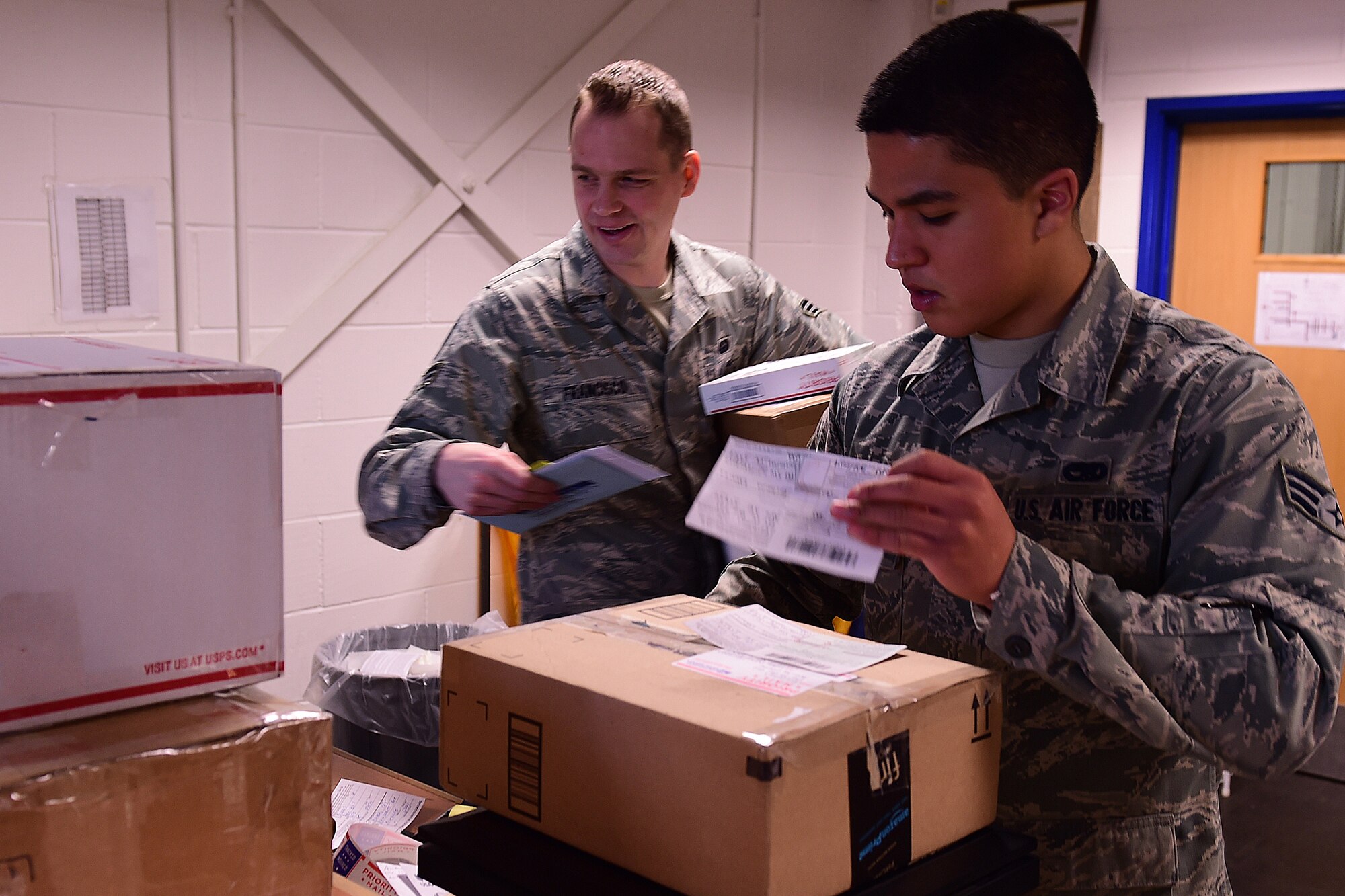 Senior Airman Jonathan Hernandez and Senior Airman Donald Francisco, both 422nd Communications Squadron postal clerks, work the front counter of the post office selling postage and retrieving packages for the customers, Dec. 2, 2014. All 501st Combat Support Wing postal offices are asking for volunteers during this holiday season. All volunteers need to fill out the appropriate forms and complete safety and lifting training prior to getting the post office specific training. (U.S. Air Force photo by Tech. Sgt. Chrissy Best)