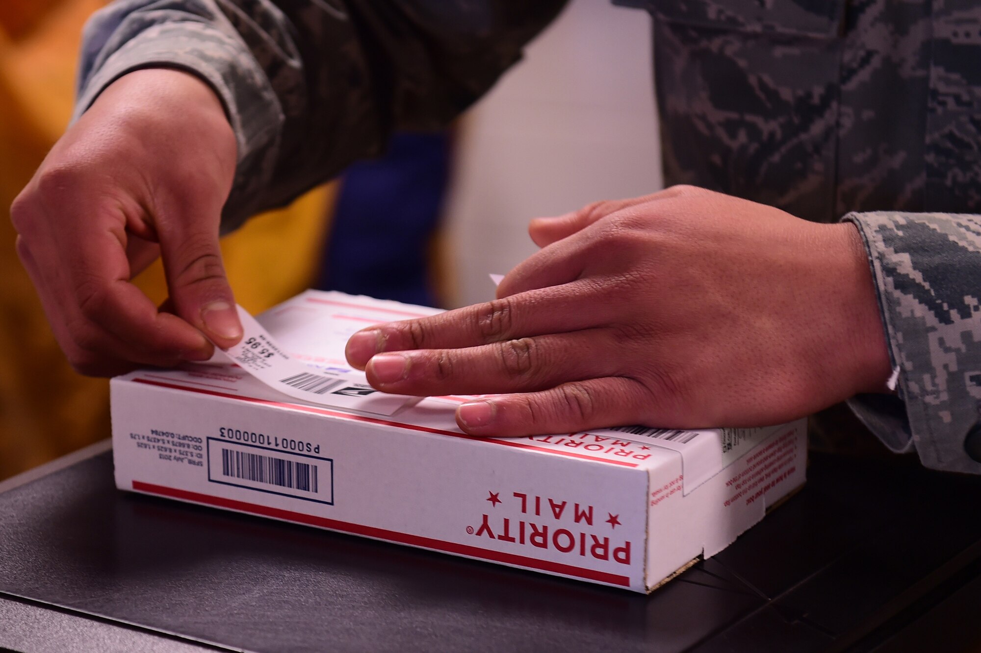 Senior Airman Jonathan Hernandez, 422nd Communication Squadron finance clerk, applies postage to a flat rate package for a customer, Dec. 5, 2014. All 501st Combat Support Wing postal offices are working extended hours during the holiday season in order to help their customers send gifts to their family and friends. (U.S. Air Force photo by Tech. Sgt. Chrissy Best)