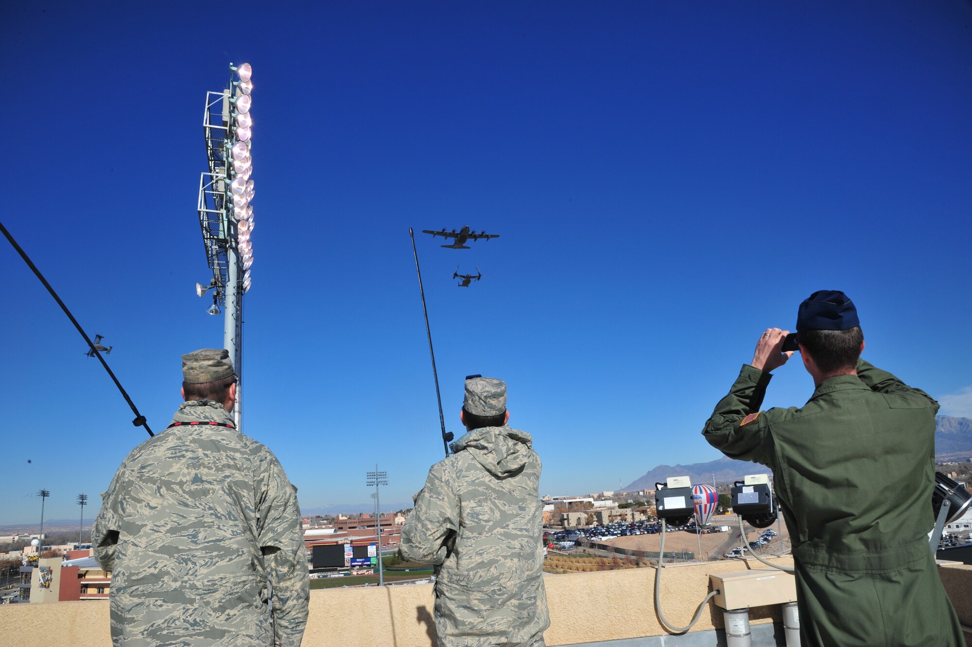 58th Operations Support Squadron members Tech. Sgt. William Carter, Senior Airman Thomas Sluski, and Capt. Michael Ward monitor an MC-130J Combat Shadow and CV-22 Osprey, from the top of the University of New Mexico's Branch Field Dec. 20. The aircraft performed a fly-by during the singing of the National Anthem to open the 2014 New Mexico Bowl. (Photo by Jim Fisher)
