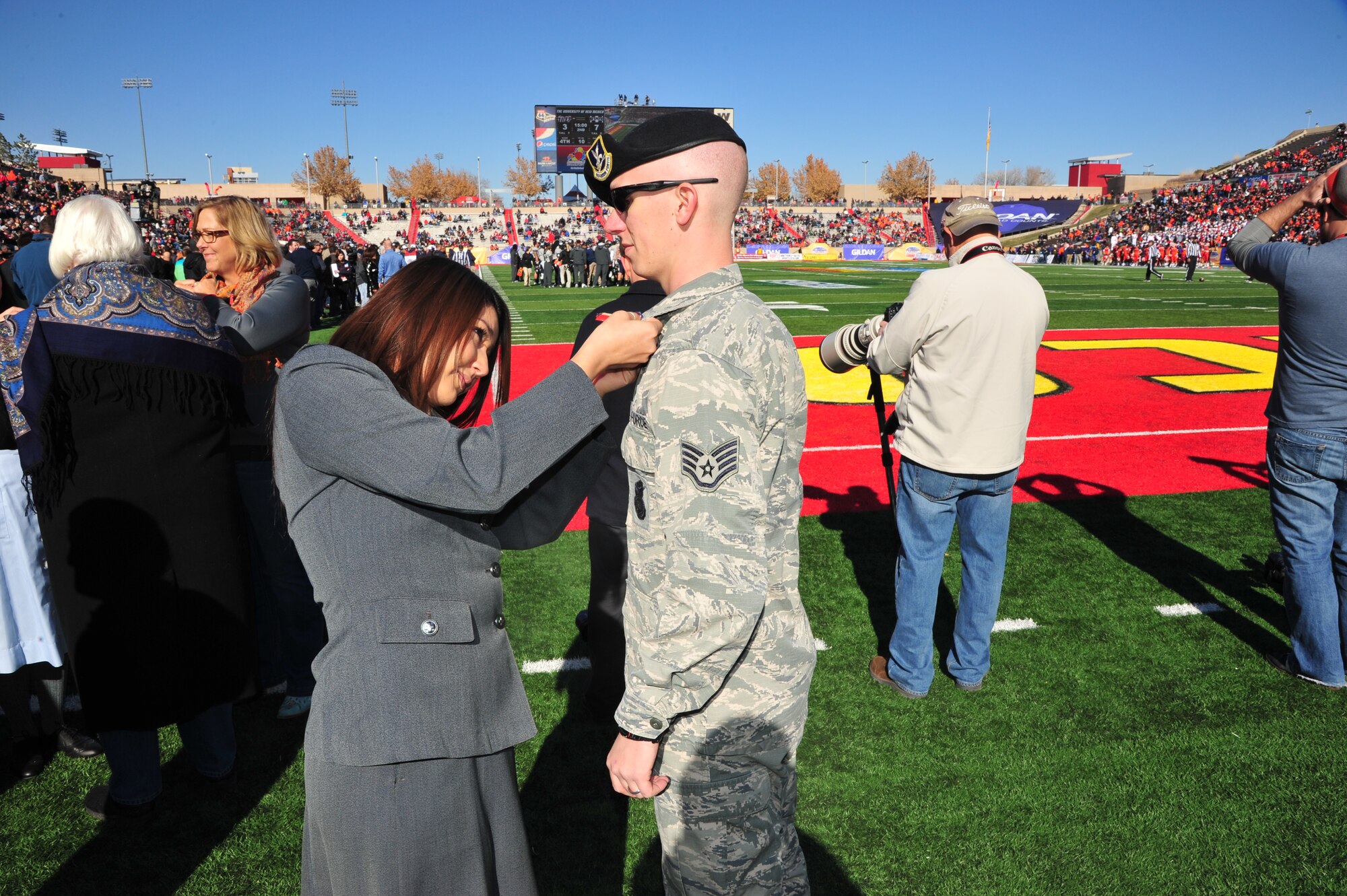 Kristin Salazar, a representative of home healthcare and hospice provider 
Ambercare, pins a Veterans Appreciation Medal on Staff Sgt. Richard Olsen, 377th Security Forces Group, at the 2014 Gildan New Mexico Bowl at the University of
New Mexico's Branch Field Dec. 20. Salazar was part of a group from Ambercare Hospice that dressed up in historical nursing uniforms as part of a tribute to veterans at
the game. (Photo by Jim Fisher)
