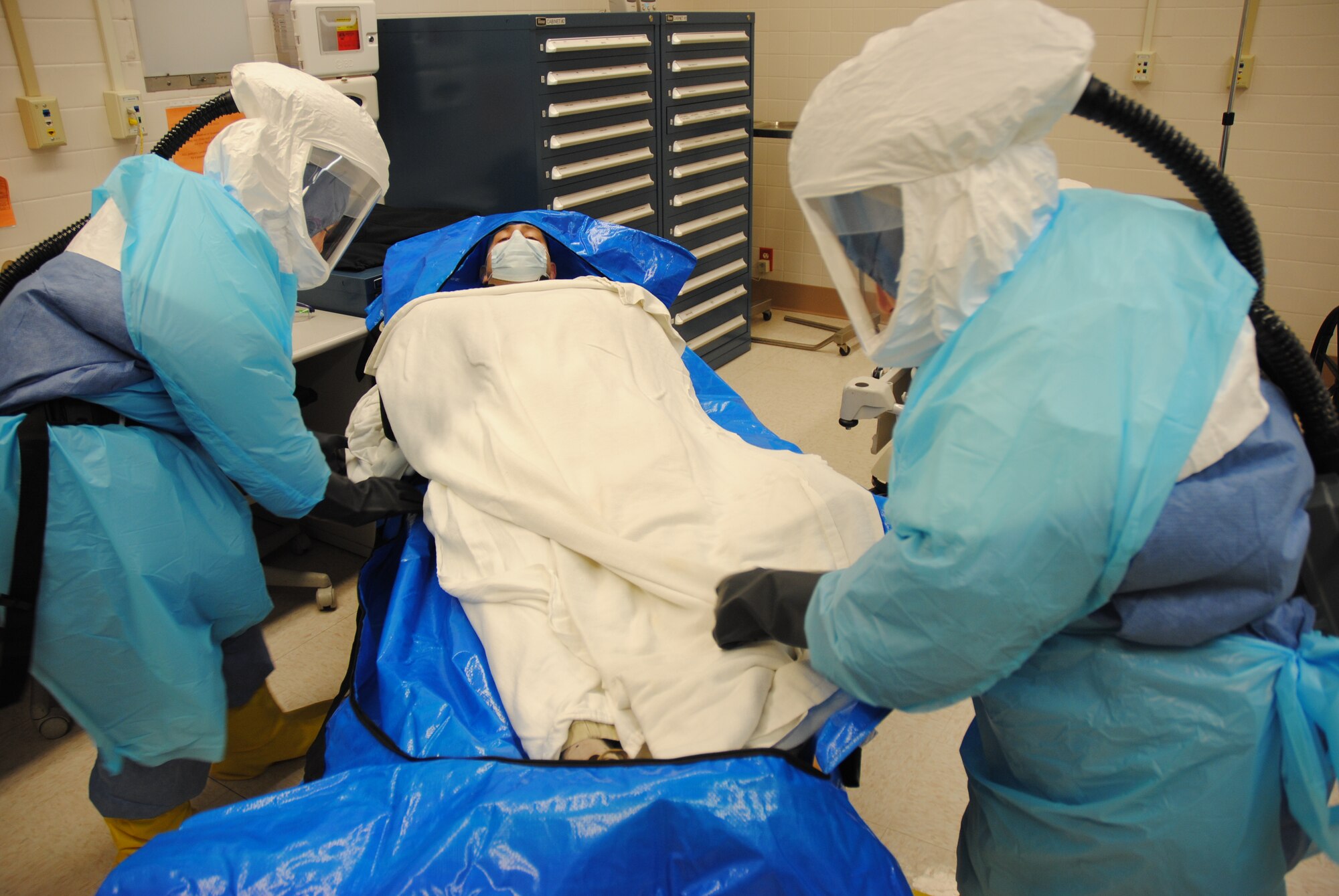 Altru paramedics Brittany Gierszewski and Val McDonald place psuedo Ebola-stricken, Master Sgt. Brian Fair, into a plastic protective covering in order to limit further exposure to the public and to safely transport him from an isolation treatment room to an ambulance waiting outside the Medical Treatment Facility on Grand Forks Air Force Base, N.D., Dec. 19, 2014. Medical personnel from both the 319th Medical Group and Altru Health Systems worked together during an Ebola Preparedness Exercise. Altru has the capability to isolate and care for suspected Ebola patients until test results were available. The base medical clinic is an outpatient facility, and does not have this capability.  (U.S. Air Force photo/Staff Sgt. Luis Loza Gutierrez)