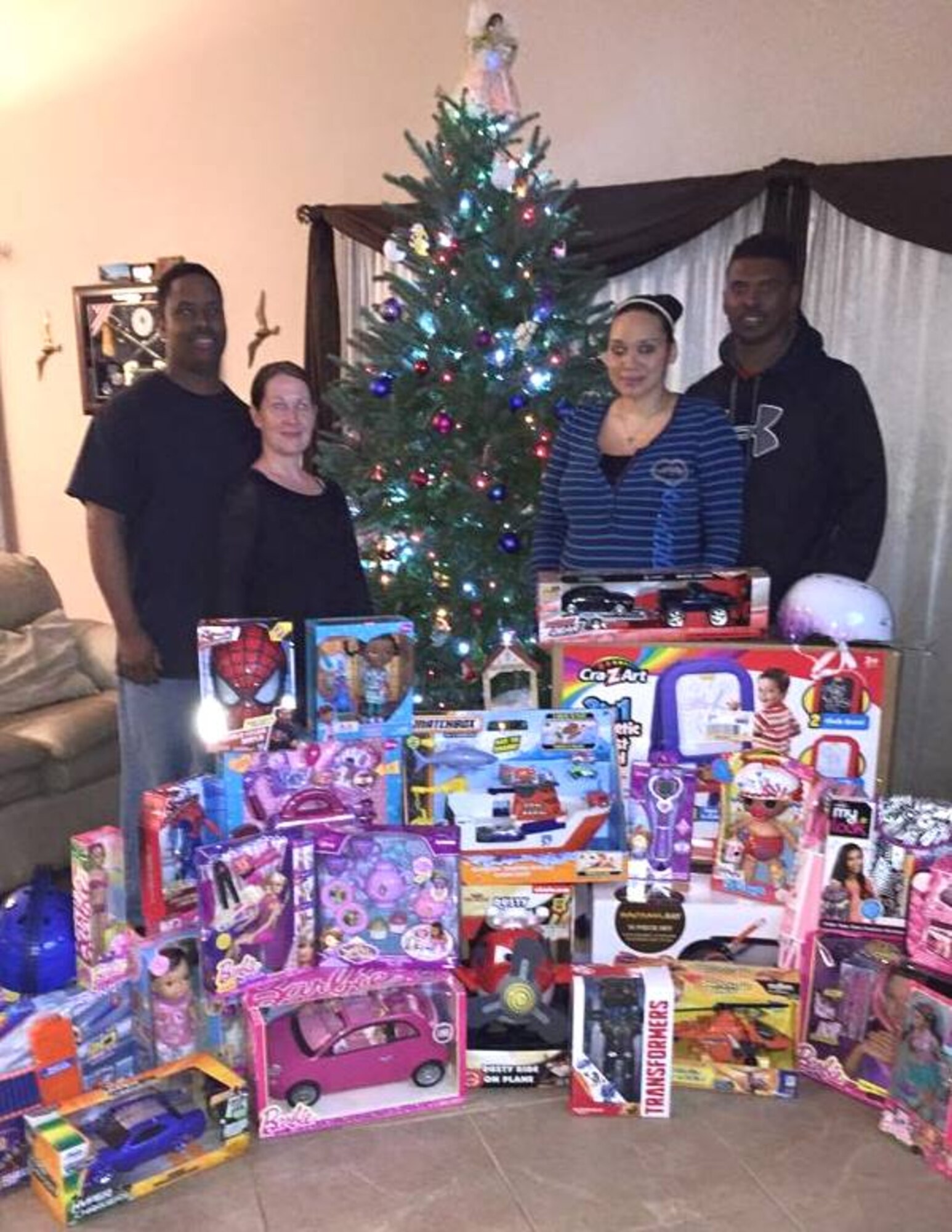 Master Sgt. Dontrel Daniels, 325th Aircraft Maintenance Squadron production superintendent, and wife Christina Daniels (left), and Staff Sgt. Gary Stewart, 95th Aircraft Maintenance Unit weapons load crew chief, and wife Michelle Stewart (right), stand by gifts donated to a family that needed some holiday cheer. The 325th AMXS holiday committee had funds left over and decided to donate what was left to a family. (U.S. Air Force courtesy photo)