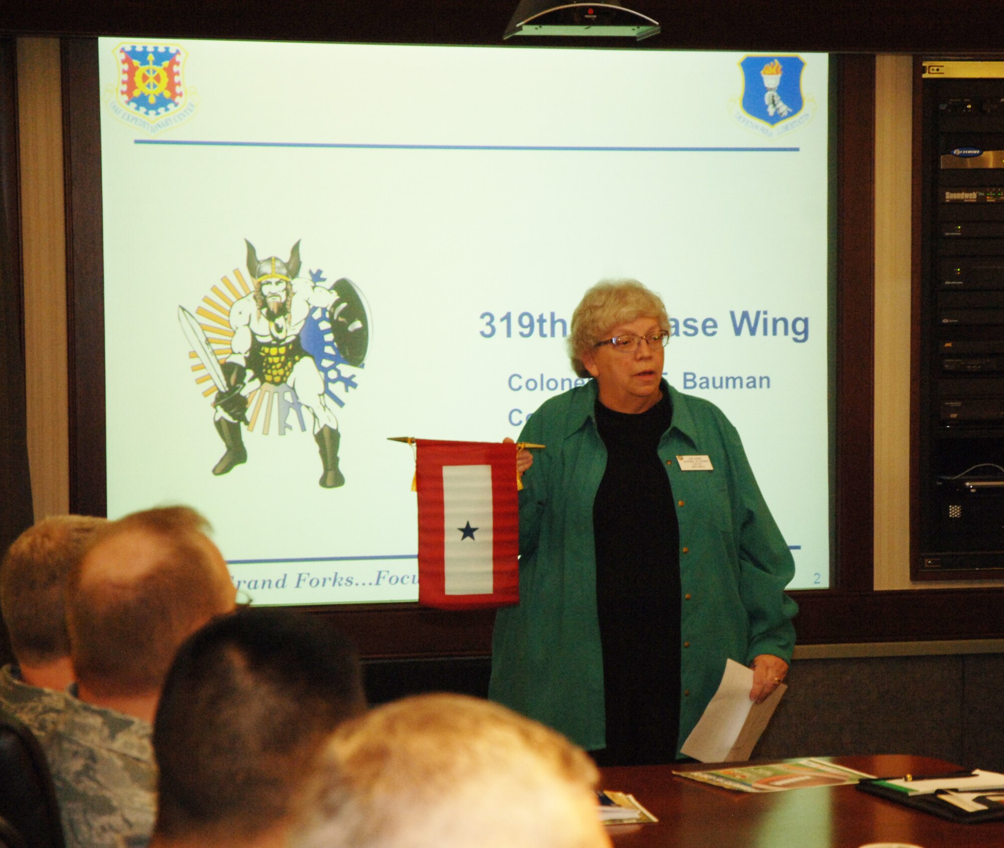 North Dakota's Department Auxiliary Vice President Diane Kraemer presents a blue star flag to wing leadership 16 Dec 14. The flag recognizes the parents of service members who are deployed and acknowledges the sacrifices they make. This flag was presented in addition to a $100 check that went towards operation warmheart, a charity that supports Airmen and their families, especially during the holiday season (U.S. Air Force photo/2nd Lt. James Fisher).
