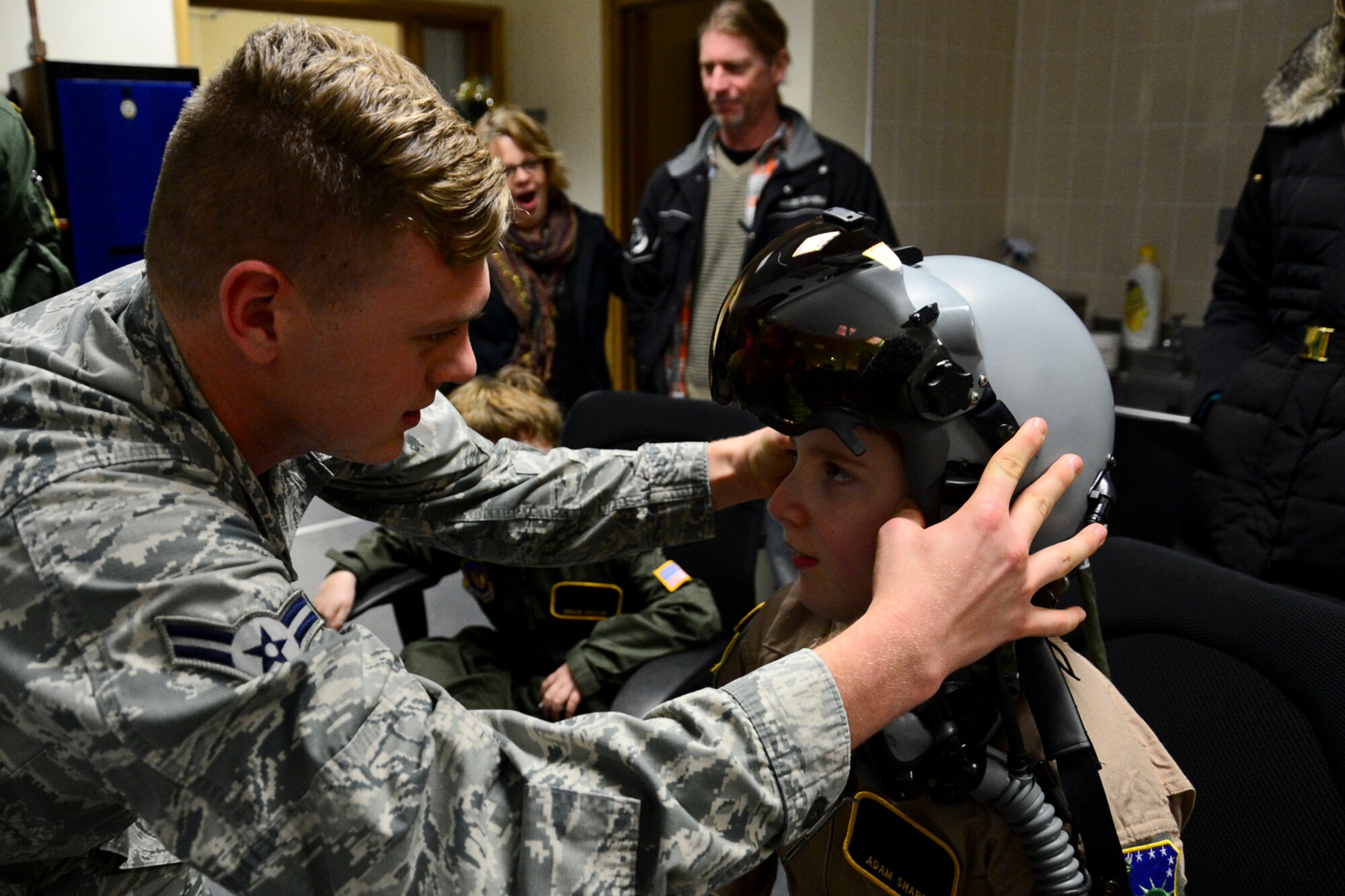 Airman 1st Class Justin Bishop, 48th Operations Support Squadron aircrew flight equipment journeyman, fits a pilot helmet on Adam Sharp during “Pilot for a Day” at Royal Air Force Lakenheath, England, Dec. 22, 2014. "Pilot for a Day" was started at RAF Lakenheath in March 2012 by Maj. Jason Bianchi, 493rd Fighter Squadron pilot, with the intent to support children throughout local communities, fighting life-threatening illnesses or conditions, by providing a day of fun and a break from routine doctor and hospital visits. (U.S. Air Force photo by Airman 1st Class Erin R. Babis/Released)