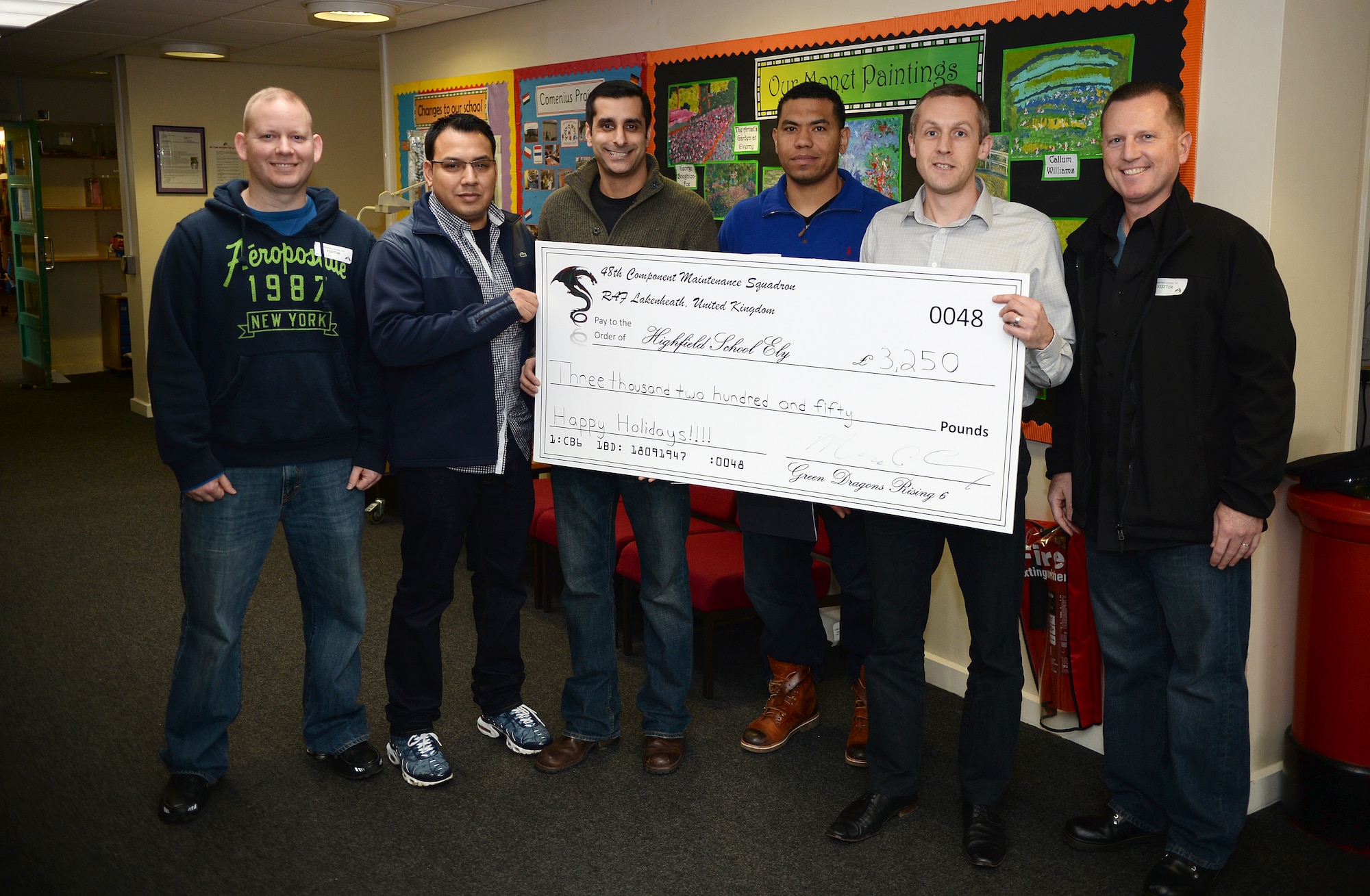 Maj. Mark Gray, right, 48th Component Maintenance Squadron commander and members of the 48th CMS Green Dragons Rising 6 present Simon Bainbridge, second from the right, Highfield head teacher, with a check for £3,250 for the school to use for their dance program at Highfield School, Ely, England. Dec. 18, 2014. Highfield is one of Cambridgeshire’s six area special education schools with 104 students in attendance. (U.S. Air Force photo by Staff Sgt. Emerson Nunez/Released)