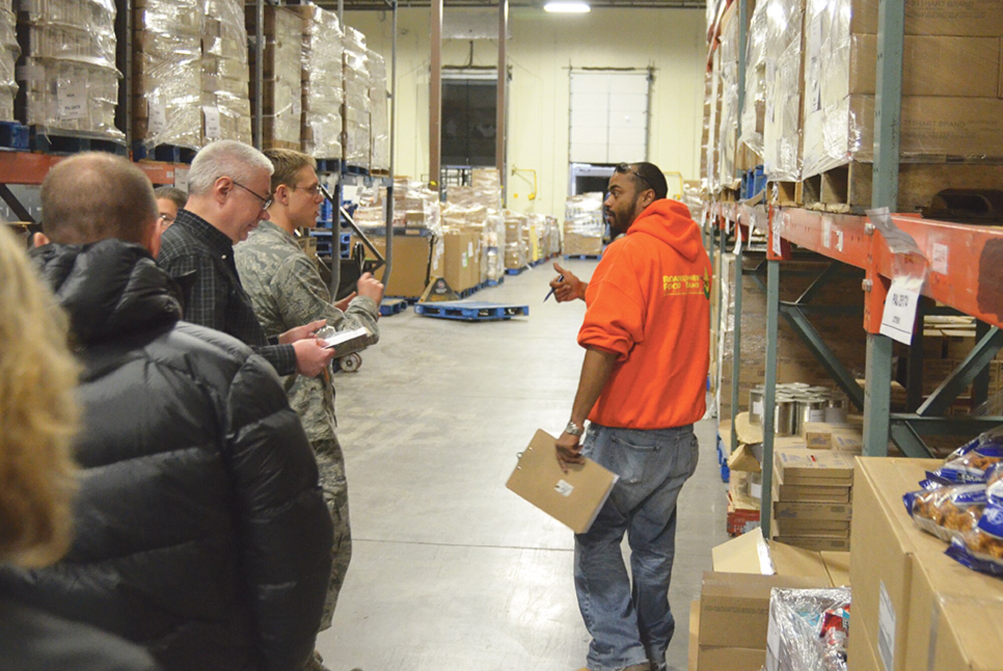 At top, from left, Capt. James Drogen, 2nd Lt. Miguel Rosario and 1st Lt. Brent Danner look for the items to fill an order at Roadrunner Food Bank. Above, Roadrunner Food Bank Distribution Manager Marc Aikin, in orange, trains a group of volunteers from Kirtland on their task.