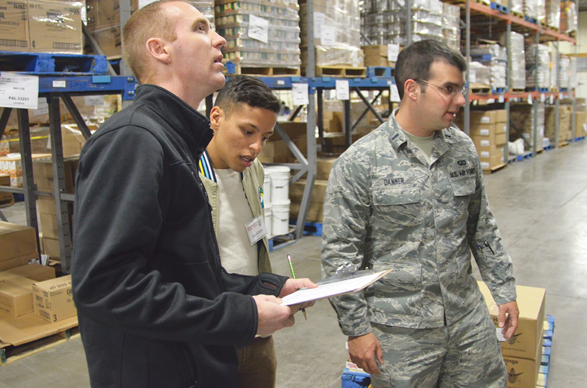 At top, from left, Capt. James Drogen, 2nd Lt. Miguel Rosario and 1st Lt. Brent Danner look for the items to fill an order at Roadrunner Food Bank. Above, Roadrunner Food Bank Distribution Manager Marc Aikin, in orange, trains a group of volunteers from Kirtland on their task (Photo by Lee Ross). 