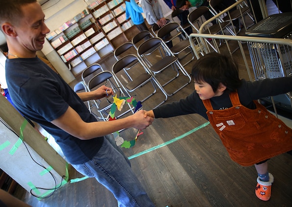 Cpl. Ruben Salinas, a resident Marine Air Ground Task Force planner for Marine Aircraft Group 12 aboard Marine Corps Air Station Iwakuni, Japan, shakes hands with a young child after receiving a handmade Christmas ornament while visiting the Akebono Orphanage in Nasake Sima, Yamaguti, Dec. 23, 2014.  As a part of giving back to the Japanese locals, MAG-12 Marines collected 777 cans of food from their unit holiday party to distribute to those in need.