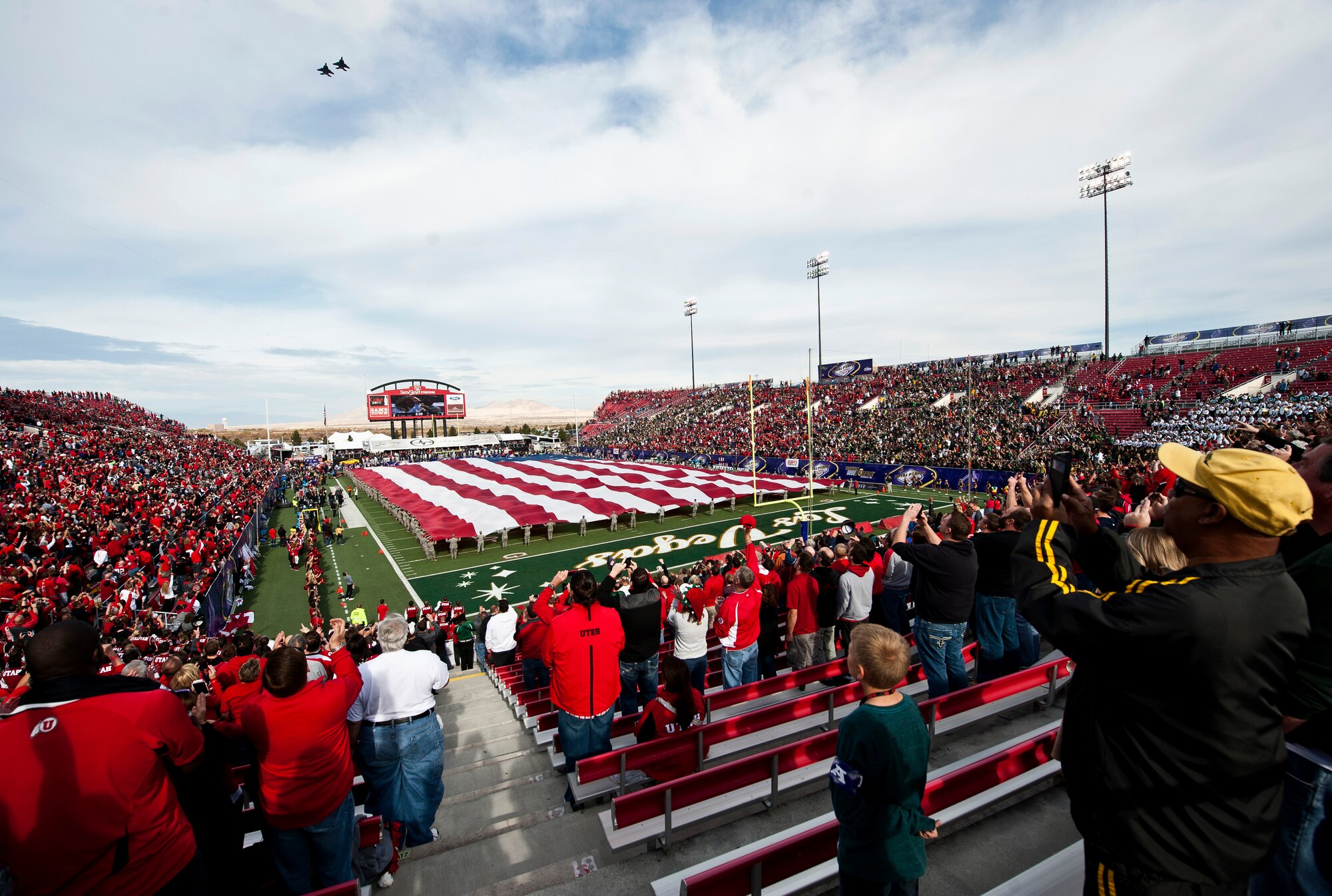Two F-15 Eagles assigned to Nellis Air Force Base fly over Sam Boyd Stadium while Airmen from Nellis and Creech AFBs hold the American flag before the start of the  Las Vegas Bowl Dec. 20, 2014. Approximately 200 Airmen volunteered to hold the flag, and then were afforded the opportunity to watch the game afterwards between the Utah Utes and Colorado State Rams. (U.S. Air Force photo by Staff Sgt. Siuta B. Ika)