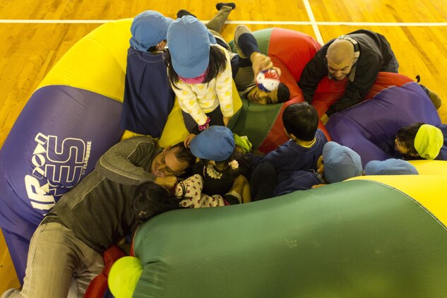 Service members aboard Marine Corps Air Station Iwakuni, Japan, play on an oversize inflatable tube with students from Ekimae Hoikuen Pre-School Jan. 28, 2014, in a community relation visit hosted by the Marine Memorial Chapel. Yasue Miyoshi, teacher with Ekimae Hoikuen Pre-School, said she noticed within the last few years the students open up to military members with their frequent visits to the school. The service members came to the pre-school to teach basic English skills to students and strengthen the Japanese-American relationship.